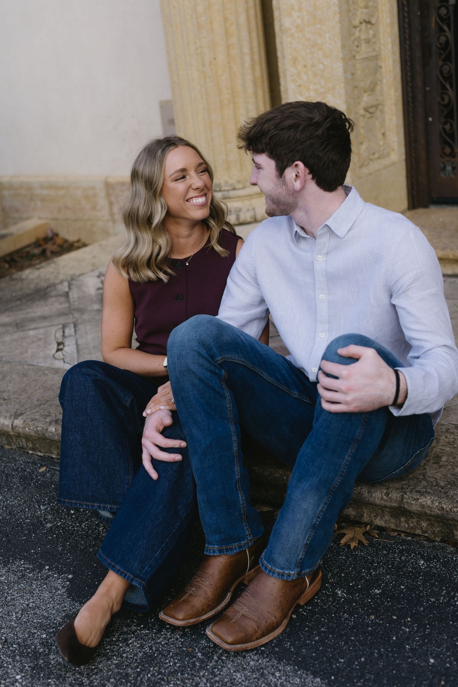 A playful couple sits together on stone steps sharing intimate moments.