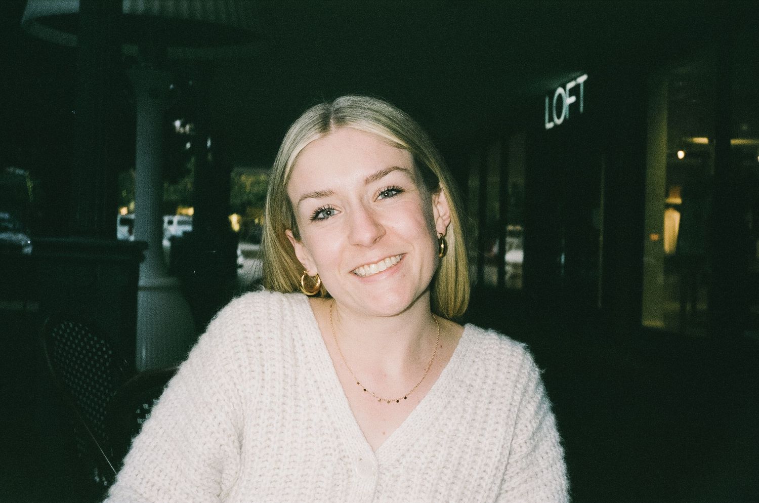 A person in white sweater posing in dark lighting conditions.