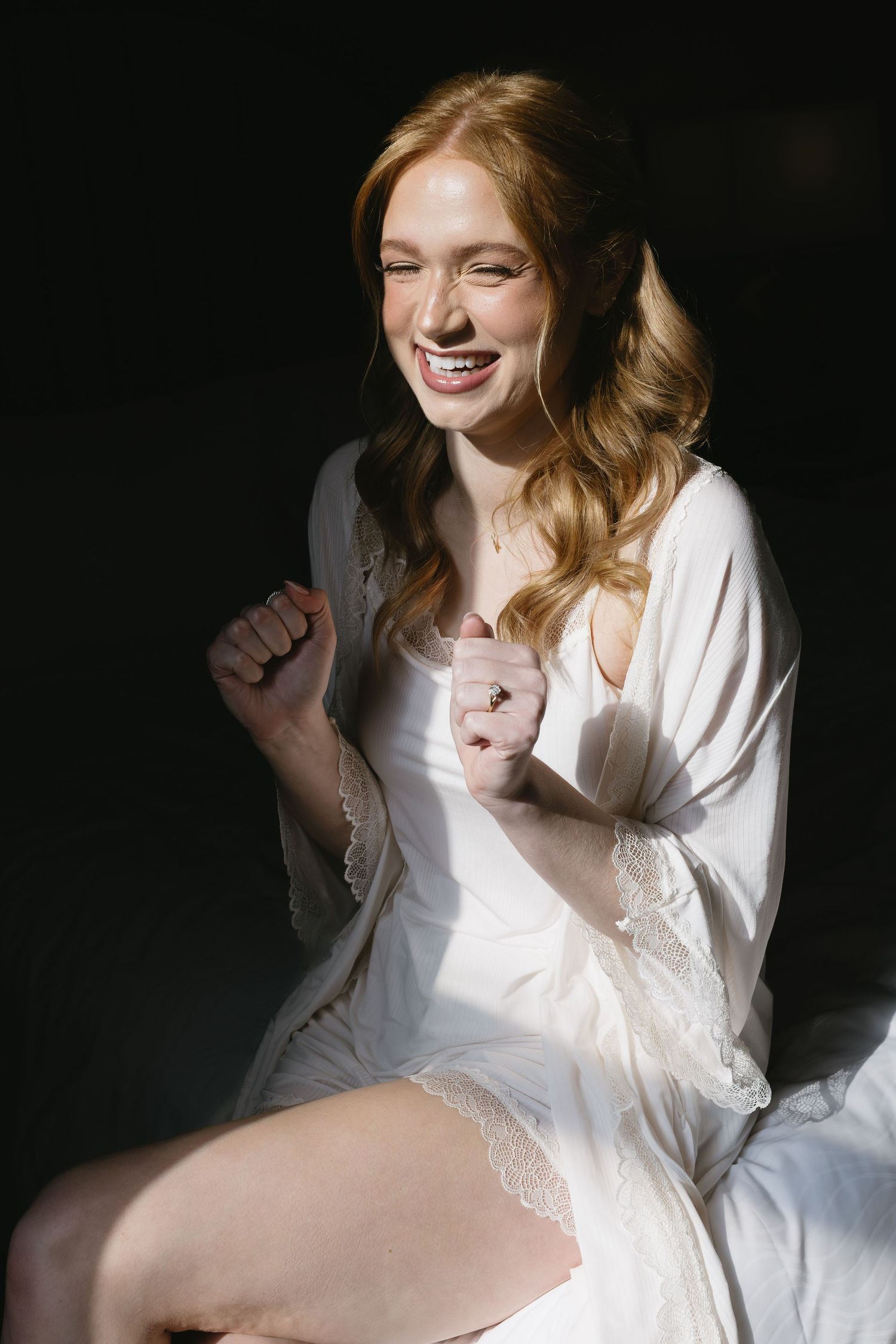 Woman in white lace robe poses playfully against dark background in boudoir photoshoot series.