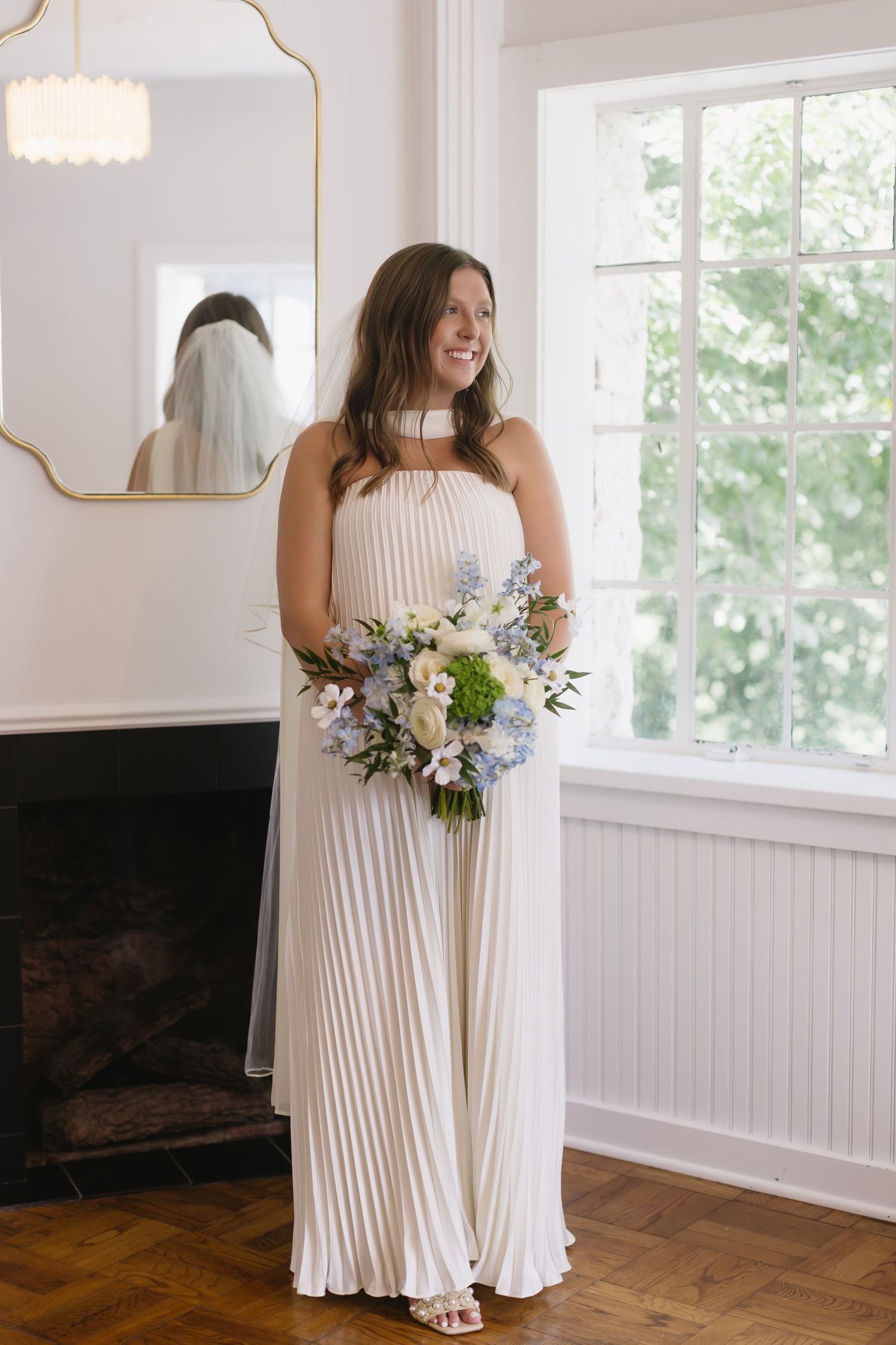 White pleated dress with floral bouquet photographed in bright interior setting.