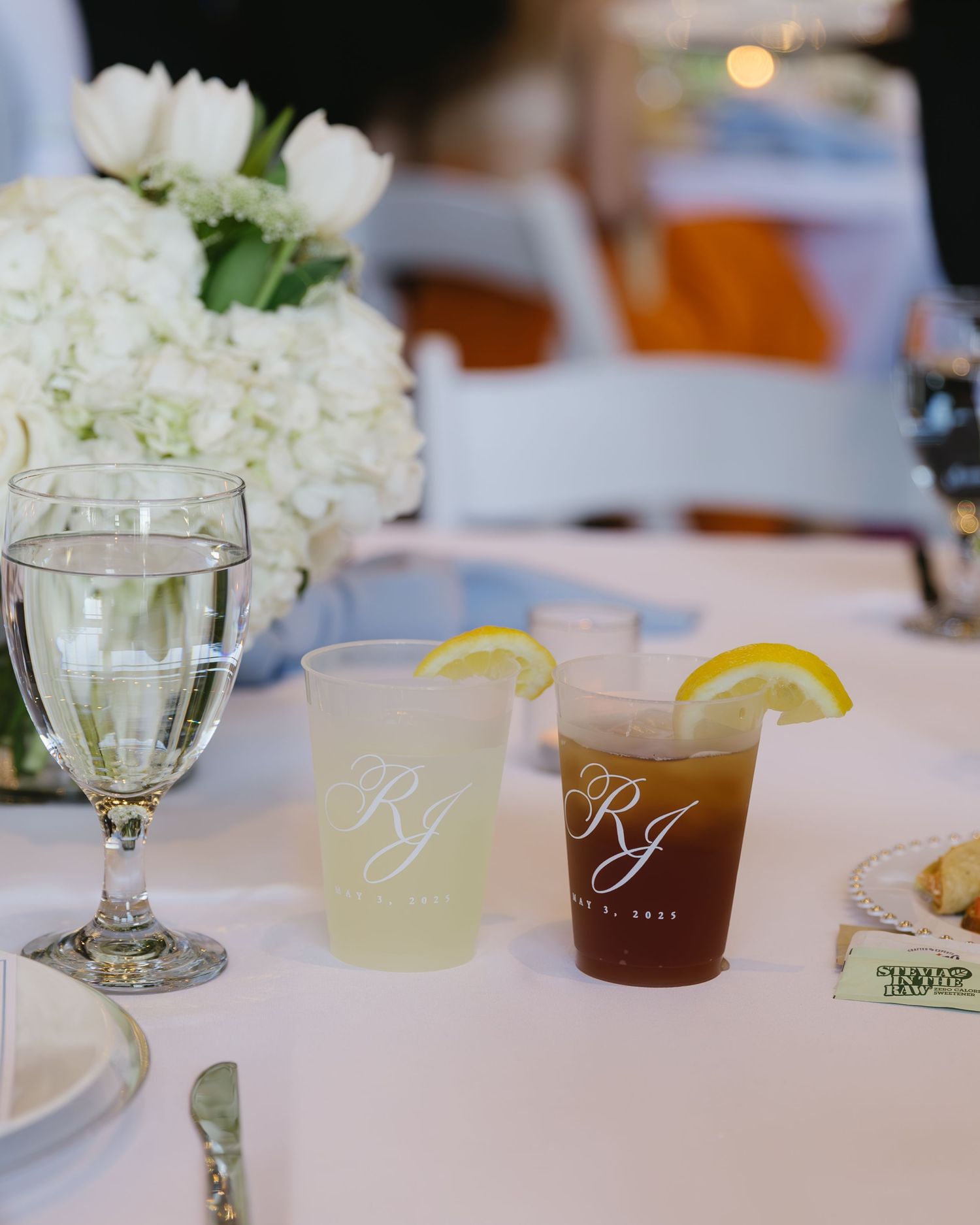 Wedding reception table settings with elegant glassware, drinks and white floral centerpieces.