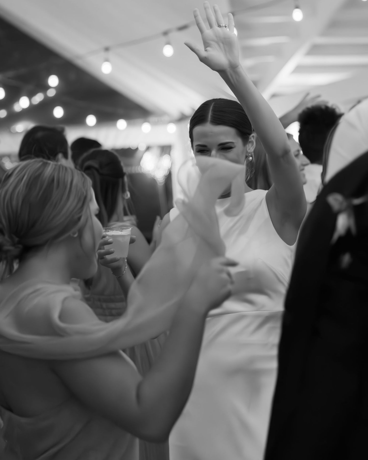 Wedding guests dancing and celebrating with raised arms on a dark dance floor.