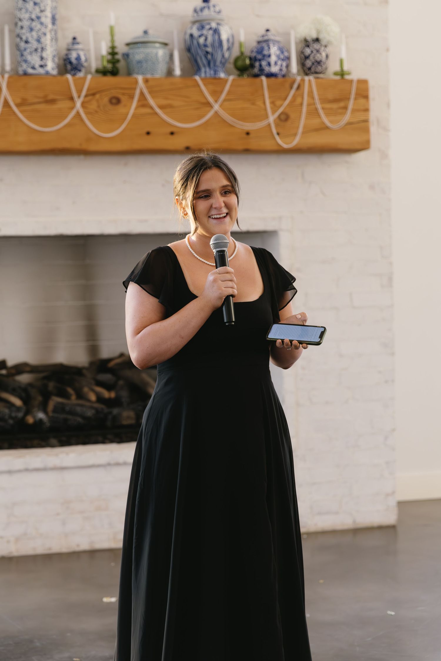 Person in black dress giving speech or toast at indoor event venue.