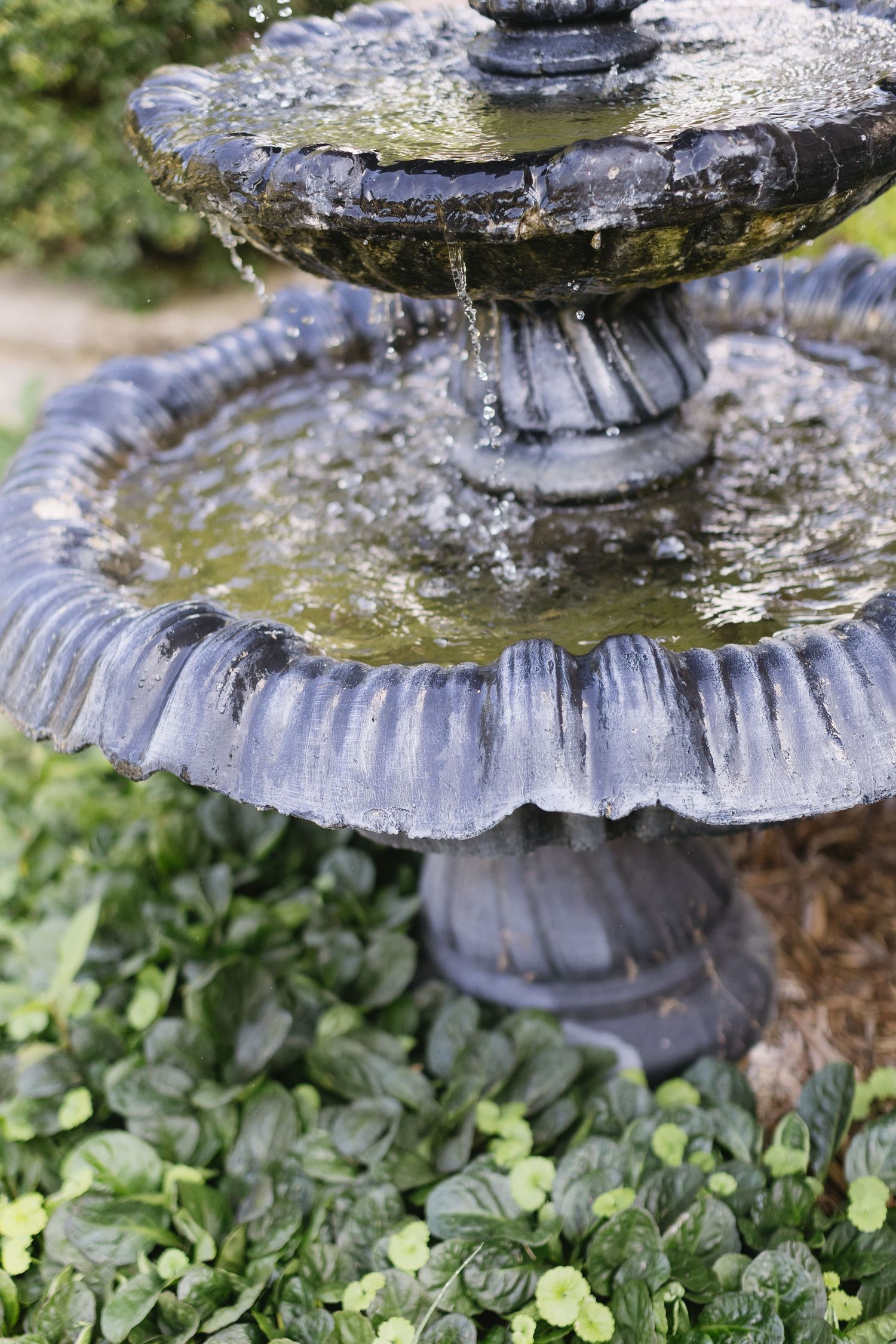 Close-up of a tiered stone garden fountain with water flowing over ornate edges.