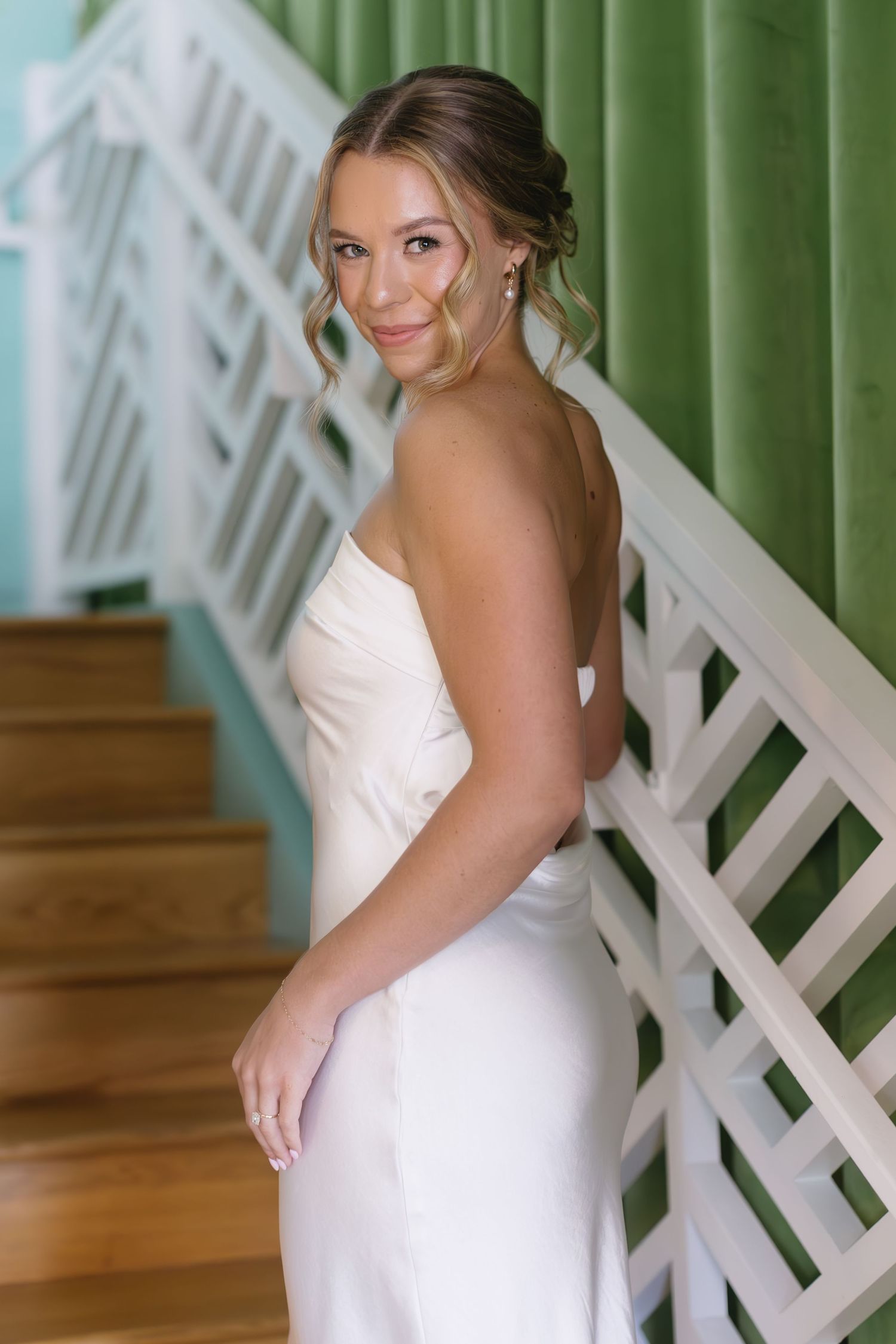 Bride in classic white gown poses elegantly against green lattice backdrop.