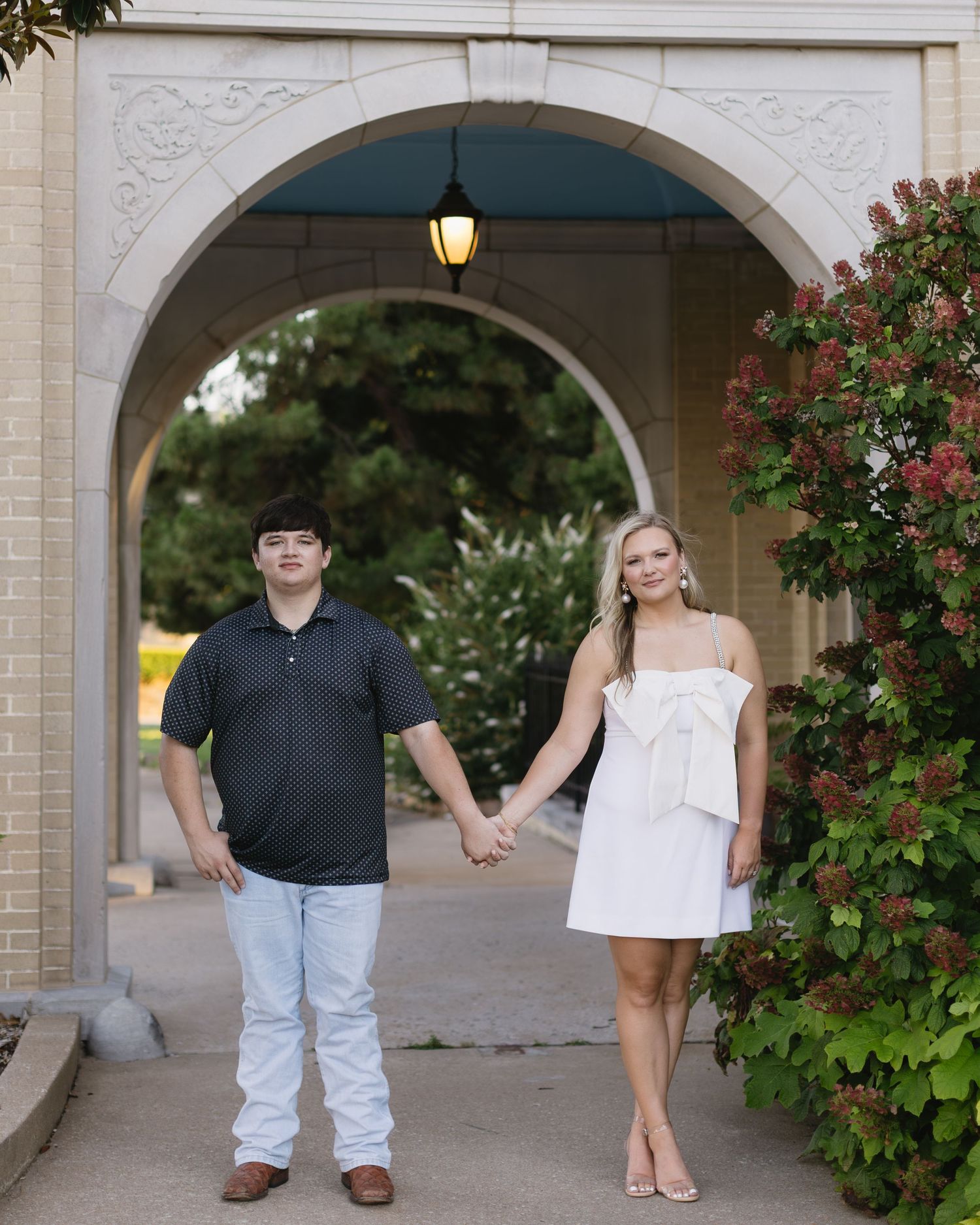 Captured series of photos showing couple posing beneath stone archway with flowers blooming nearby.