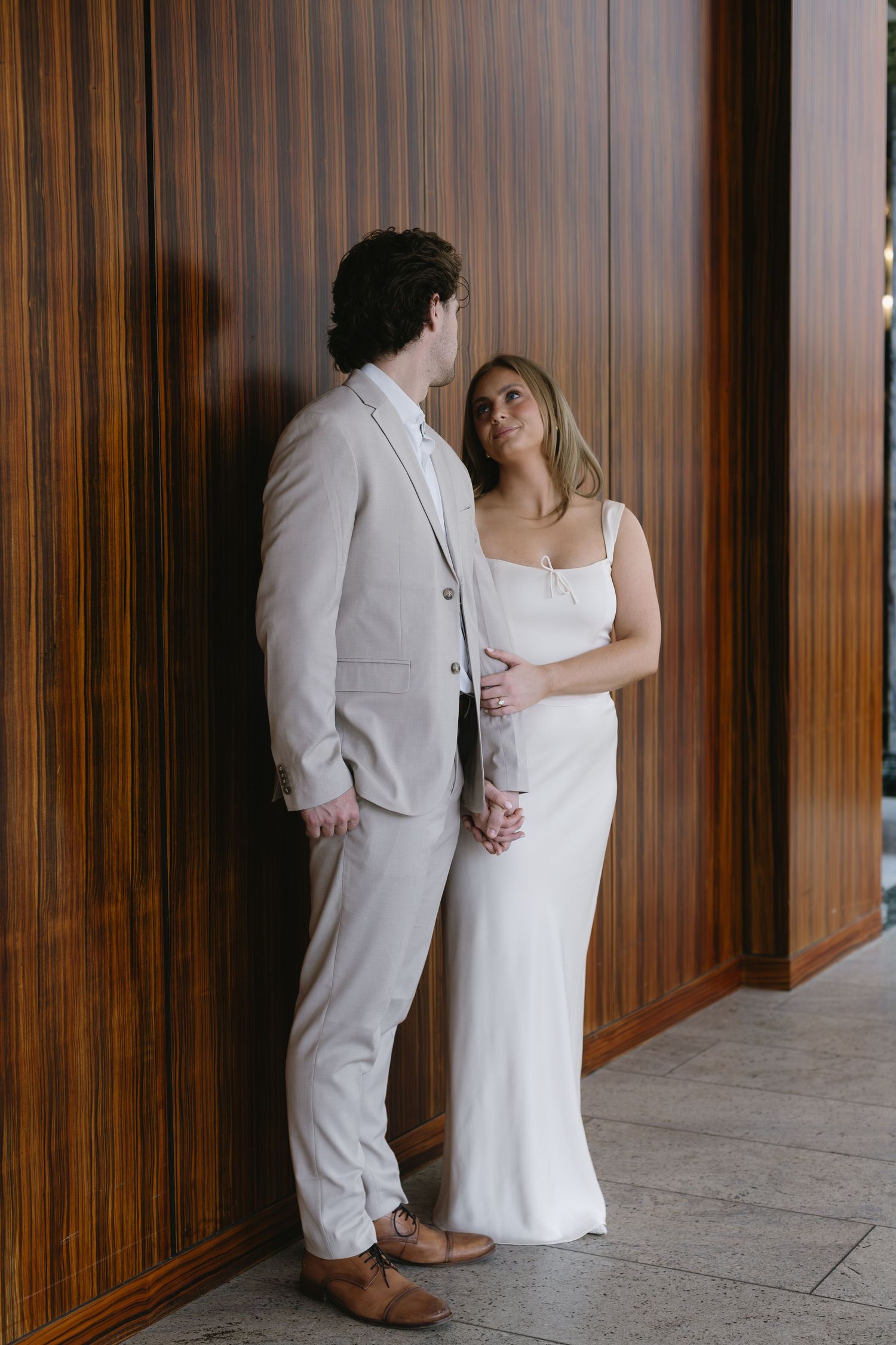 Intimate moment between couple in white and beige attire against wooden paneled wall.