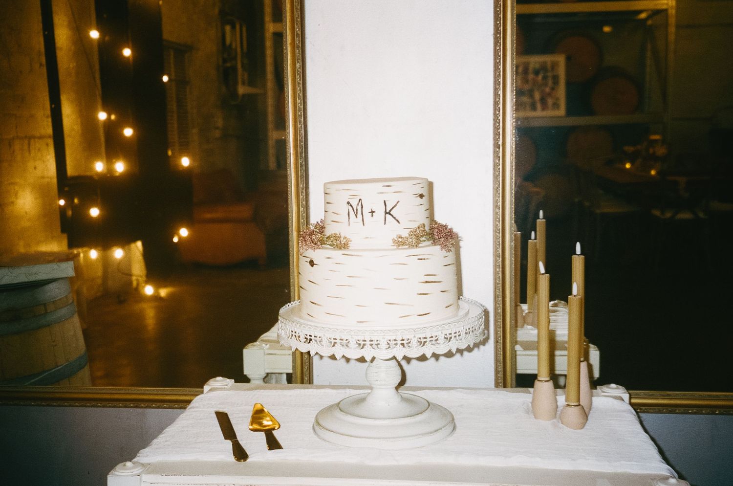 White wedding cake display with gold candles and romantic lighting in an indoor venue.