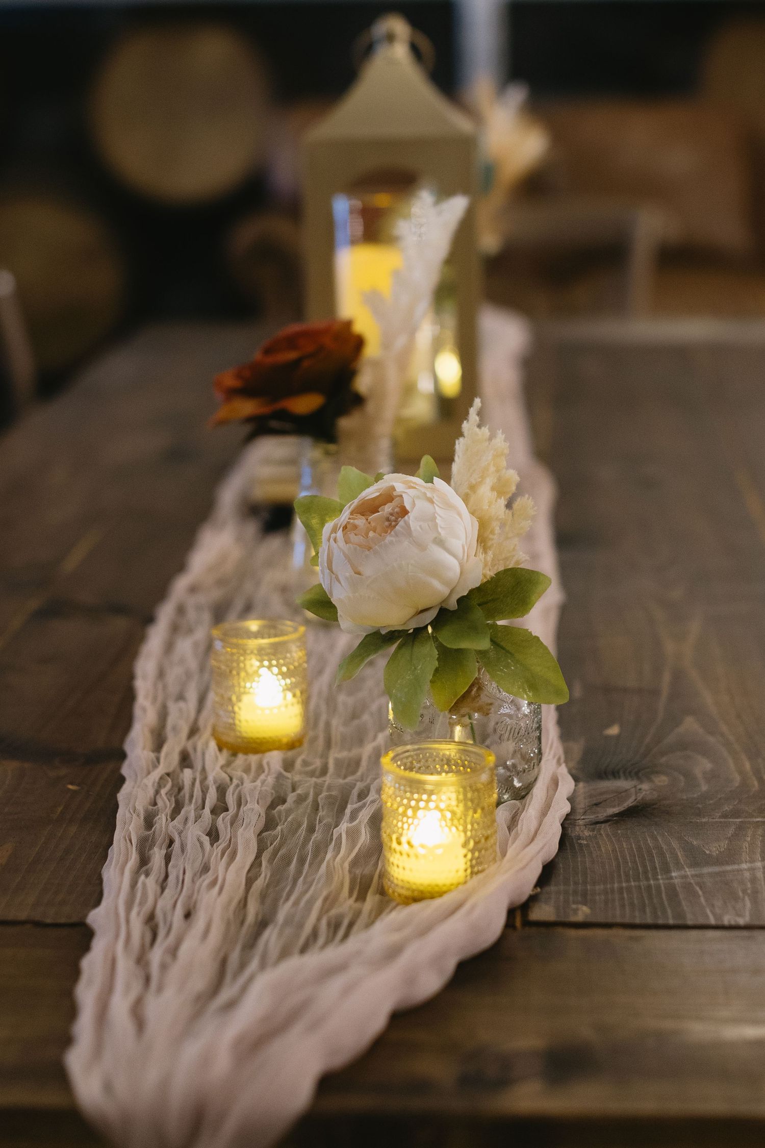 Candlelit table runner with white lace and greenery creating an intimate dining atmosphere.