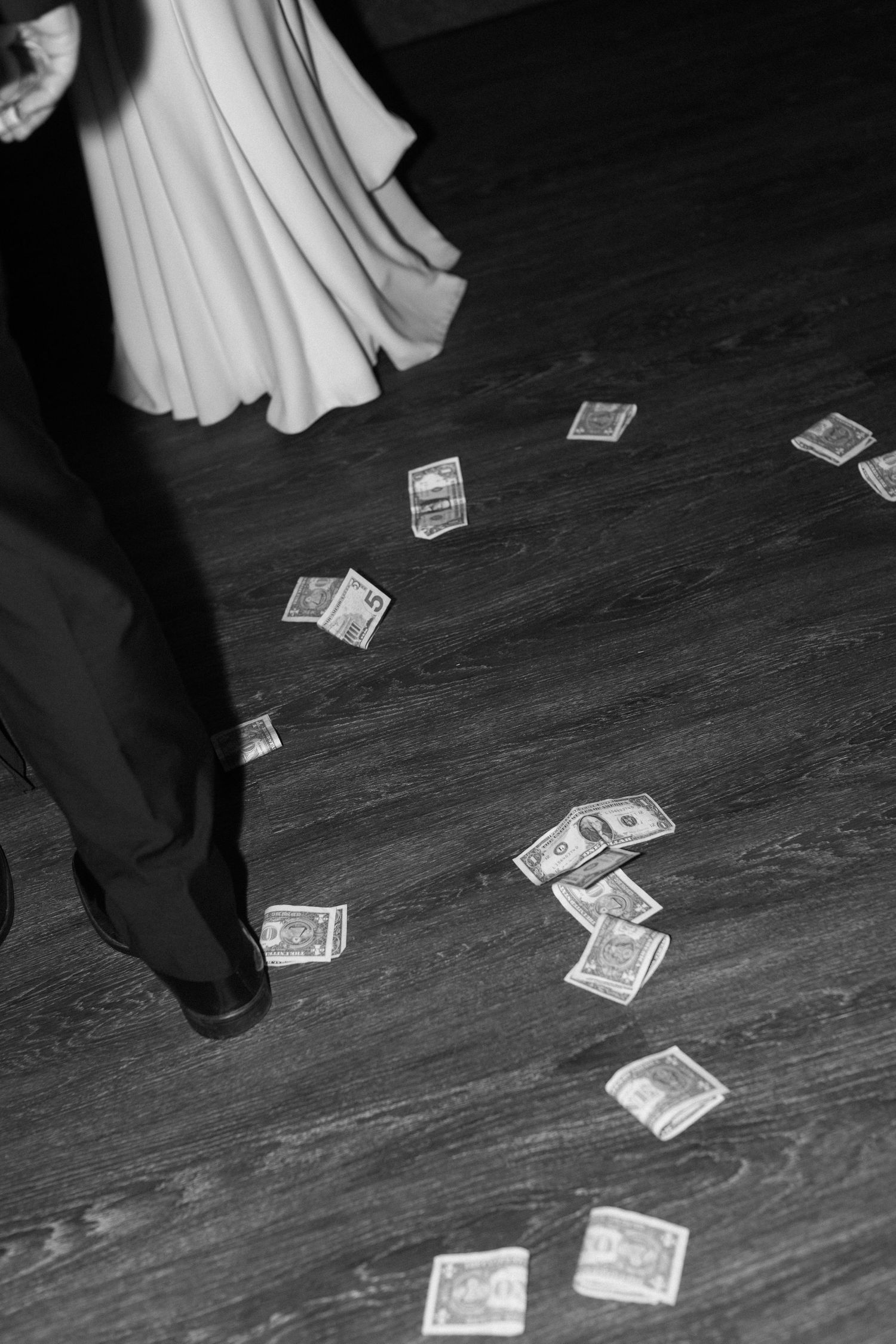 Black and white photo of dollar bills scattered on dark wooden dance floor.
