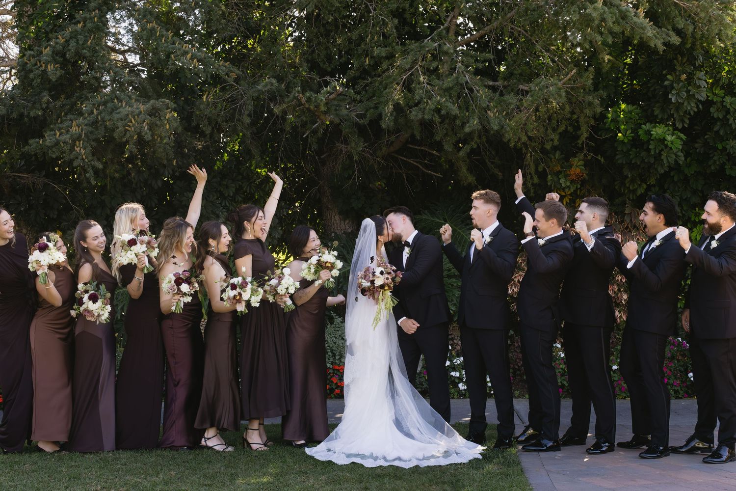 Wedding party in black and white attire poses for formal group photos on a grassy lawn.