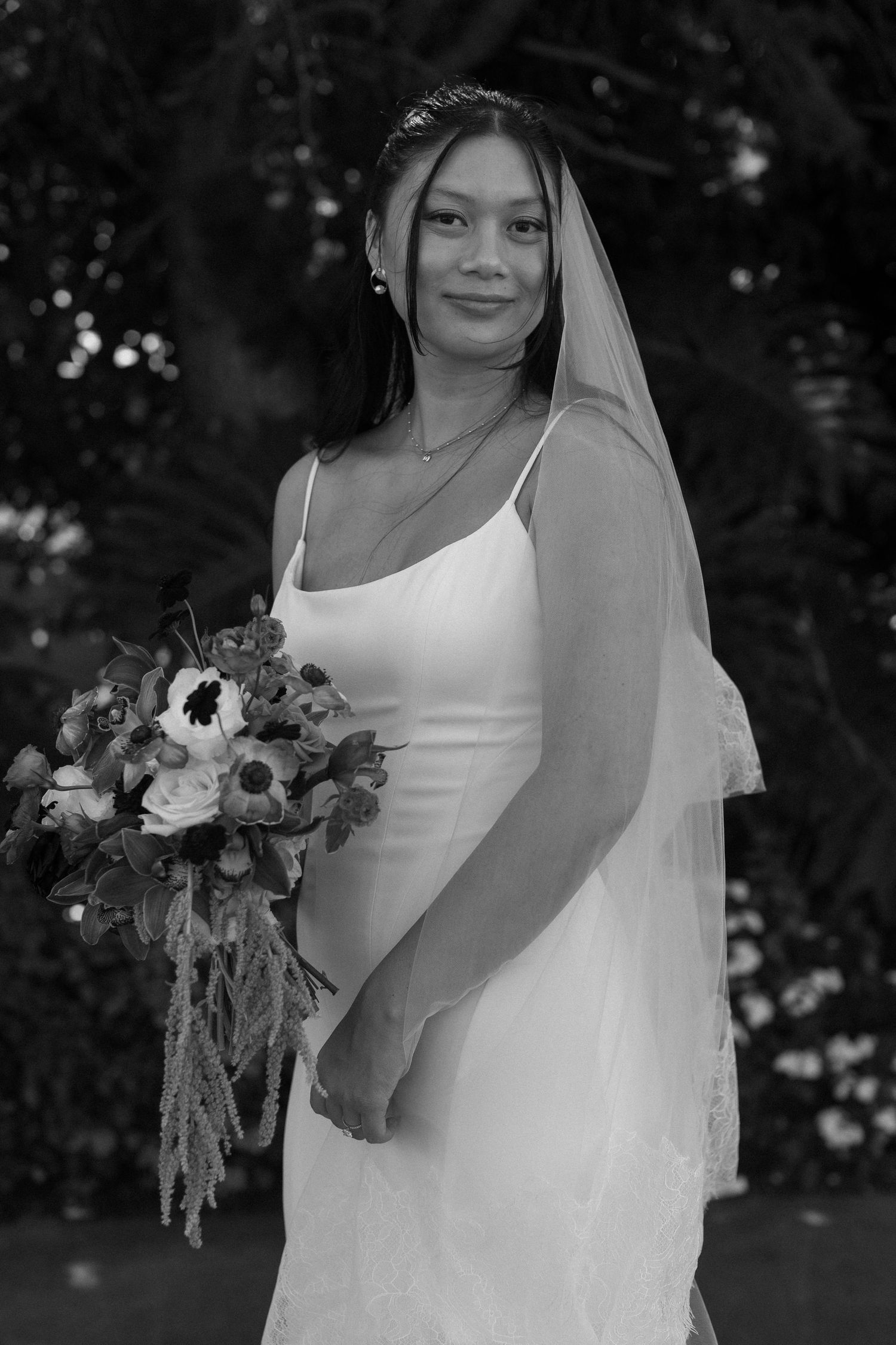 Bride in elegant white dress holds beautiful floral bouquet in black and white portrait series.