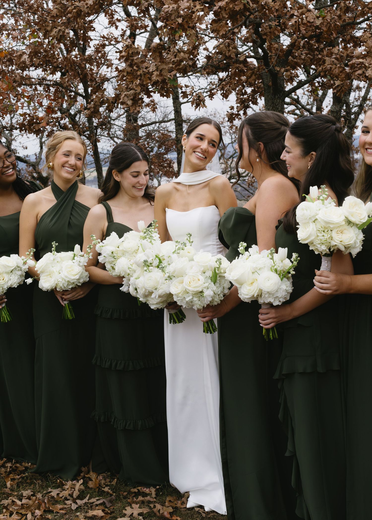 Wedding party in black and white attire holding bouquets while standing in a line outdoors.