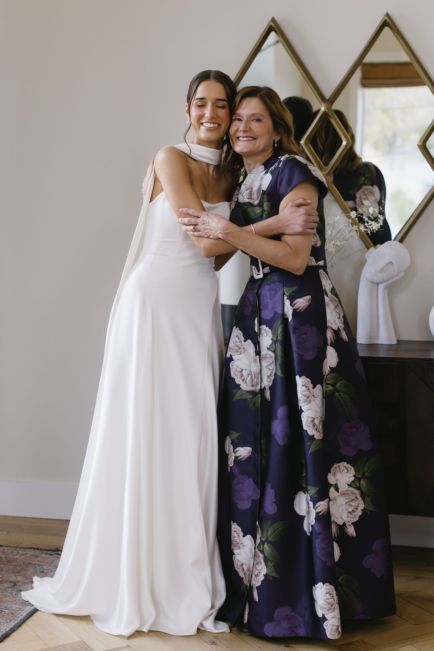 Wedding scene with people embracing, one wearing a white gown and another in a floral purple dress.