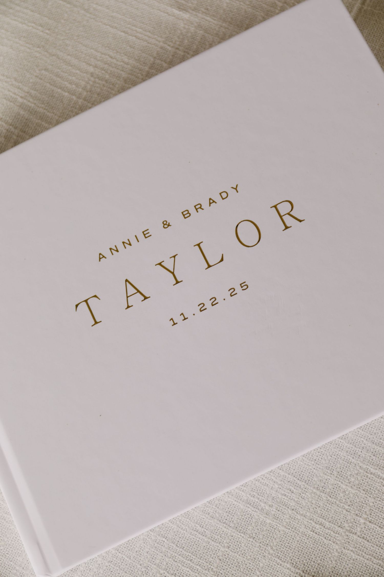 Elegant white wedding album with gold text showing names and date.