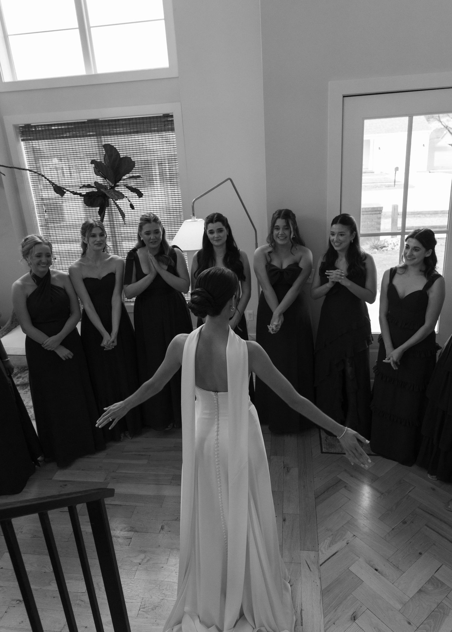 Wedding party in black dresses forms a circle around the bride in white.