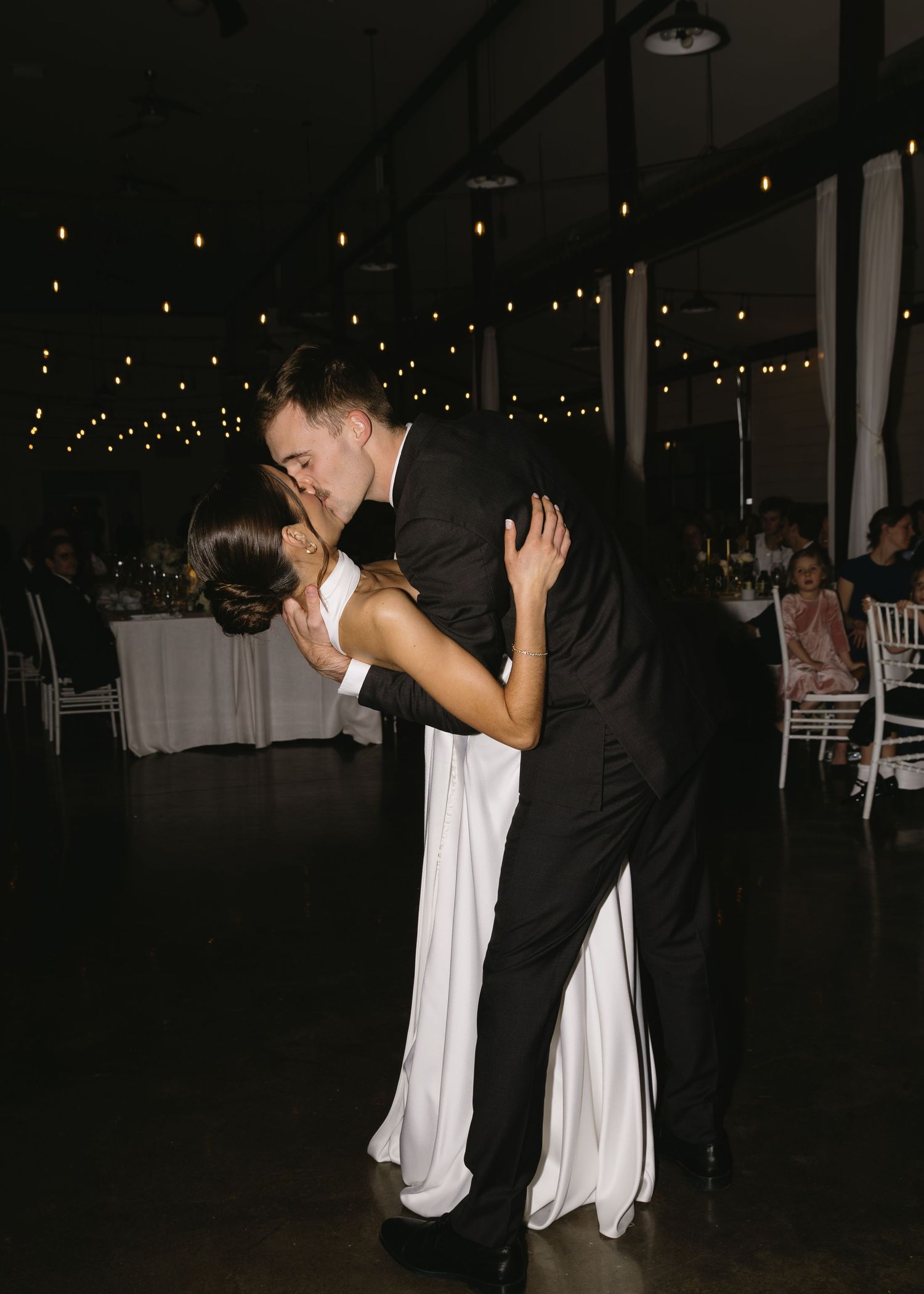 Wedding reception dance floor with couples dancing under dim lighting and string lights.