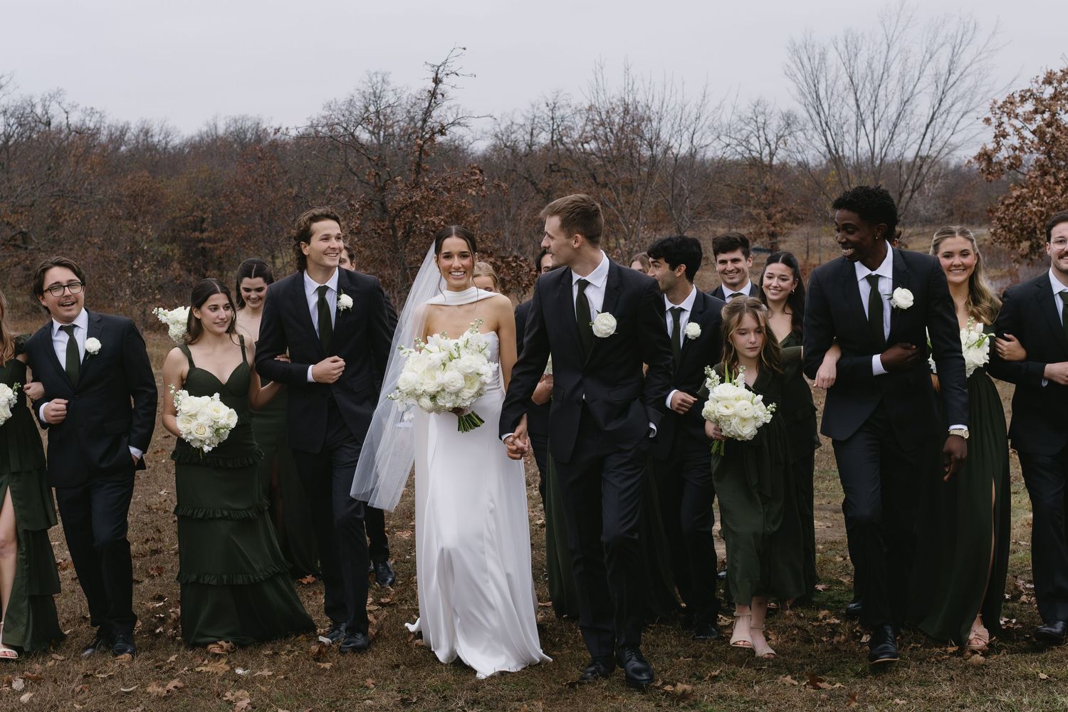 Wedding party walking together outdoors on a fall day wearing formal black attire and white dresses.