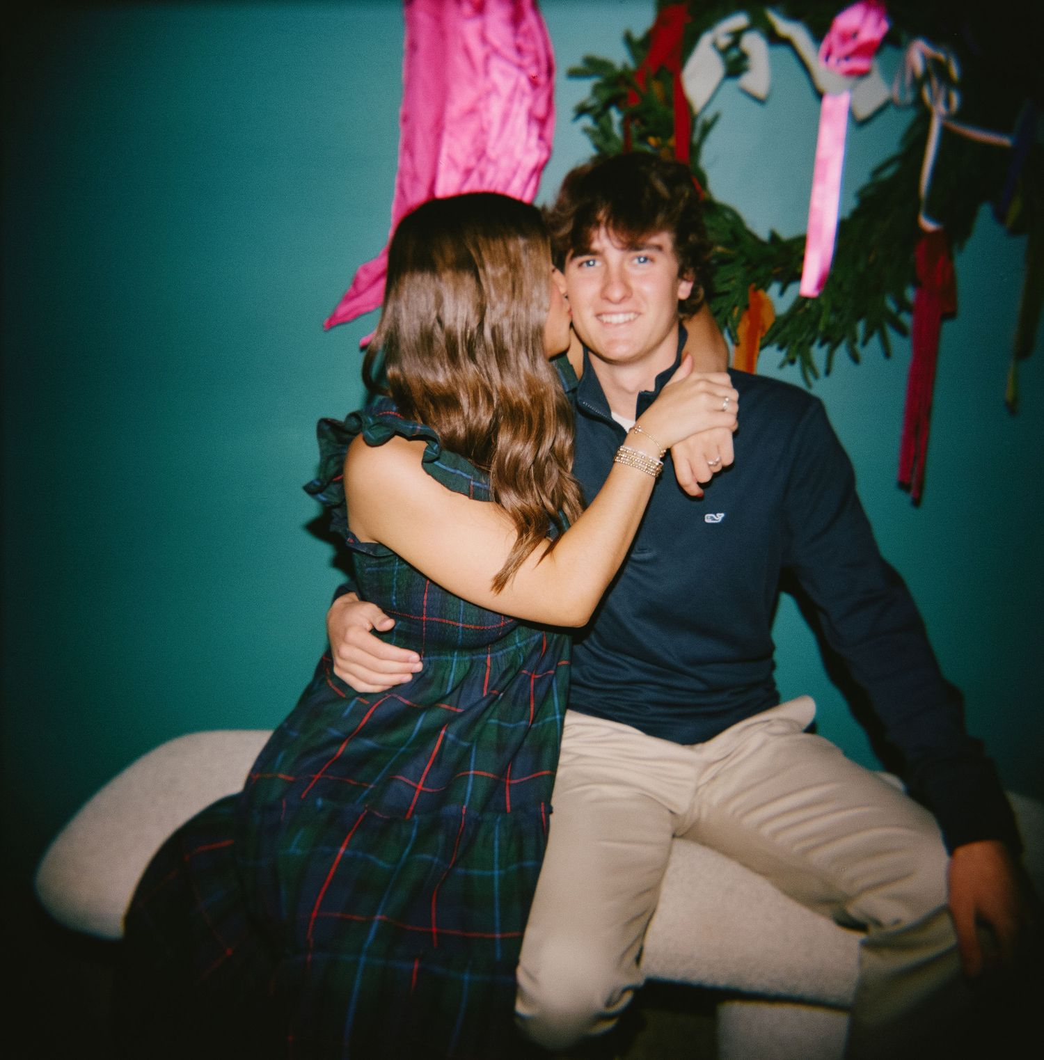 Couple shares a tender moment on a couch with teal walls and holiday decorations in the background.
