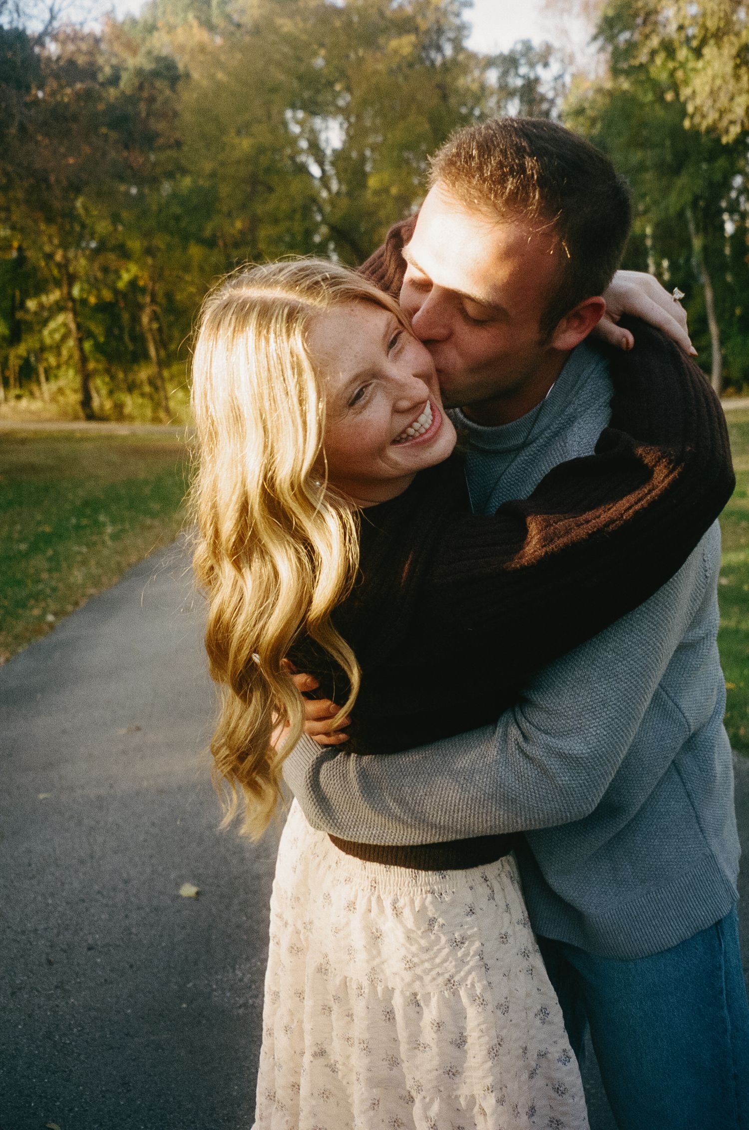 A romantic couple embraces and shares tender moments along a tree-lined autumn path in the park.