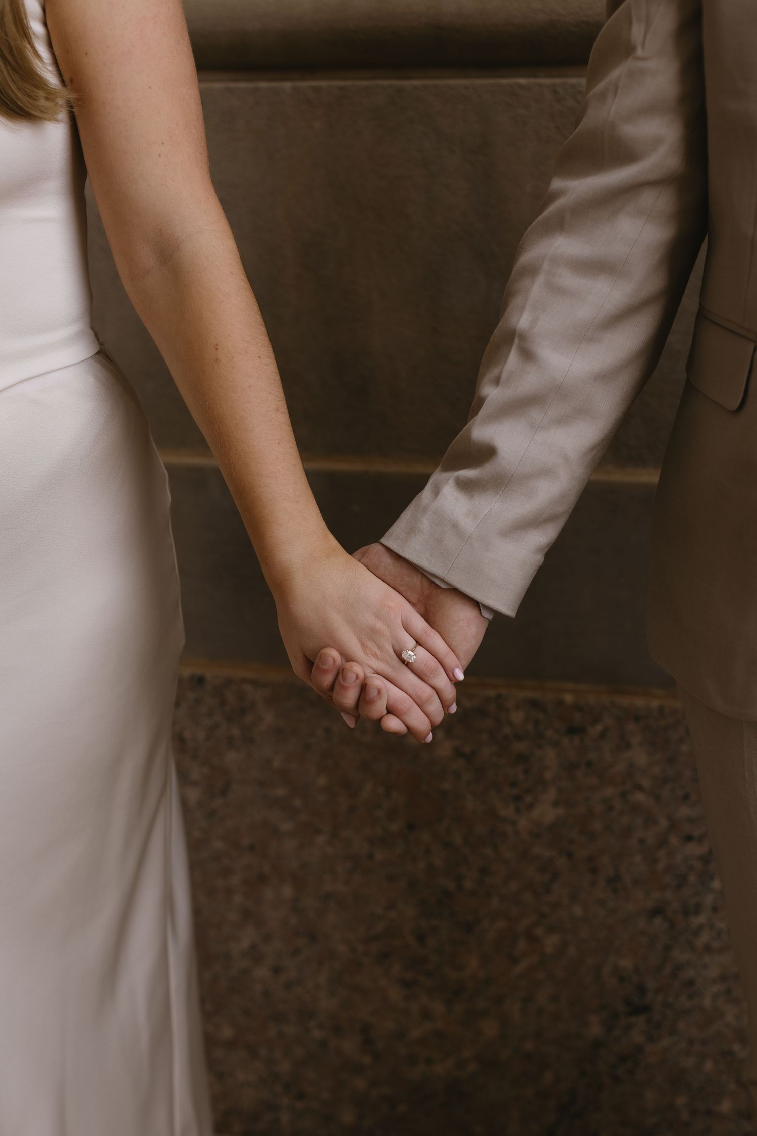 Close-up of couple holding hands while wearing formal beige and white attire.