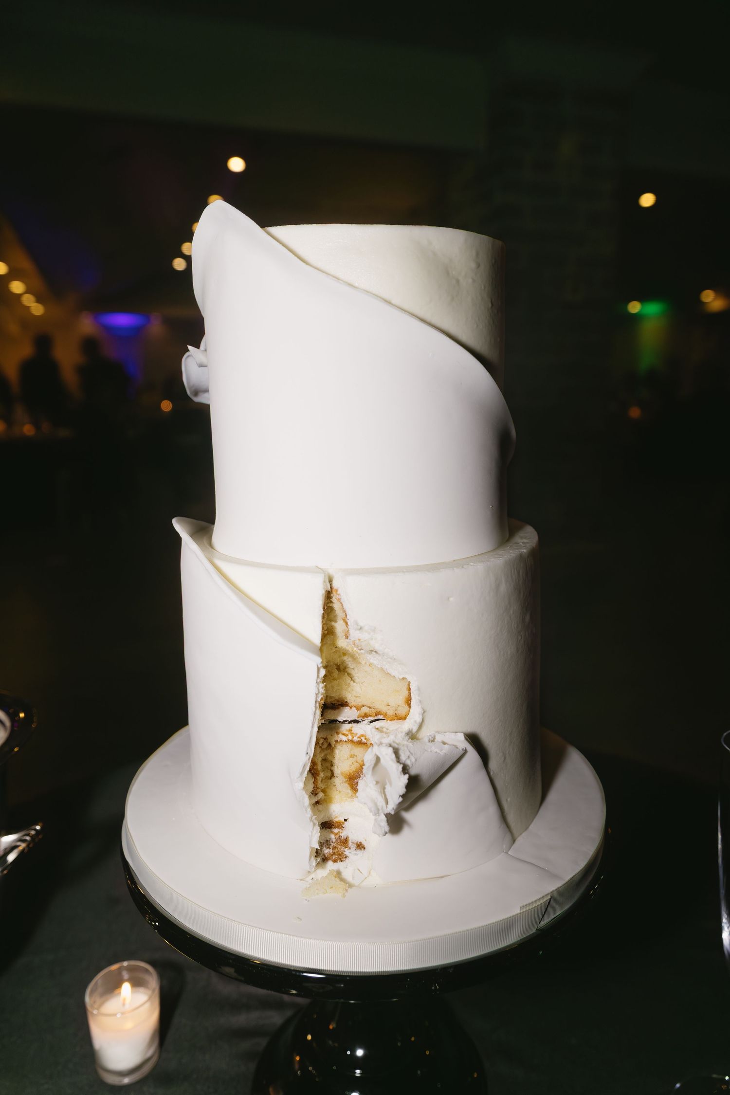 Damaged white wedding cake in dark lighting with candlelight.