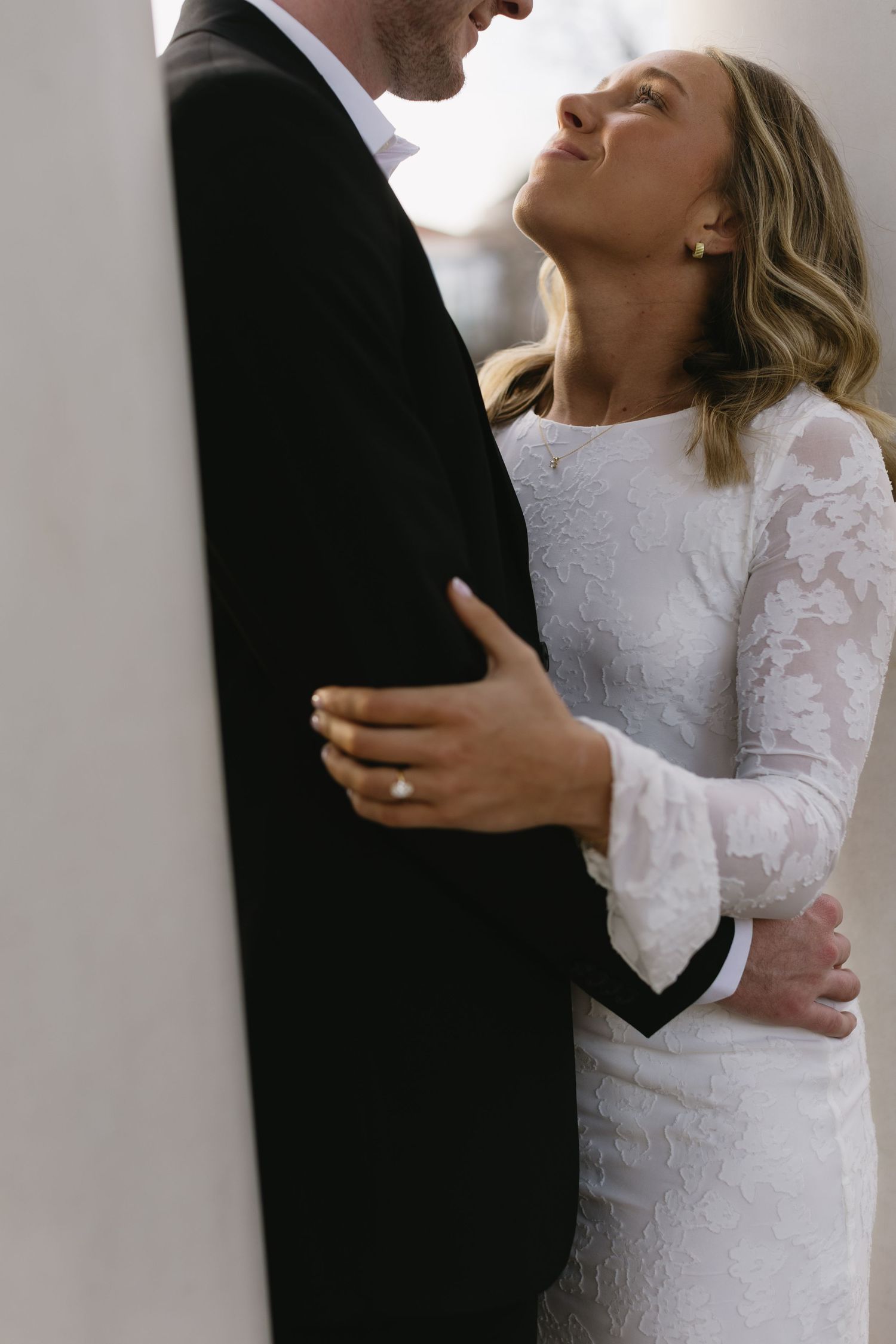 Intimate portrait of a couple in wedding attire embracing against a white wall.