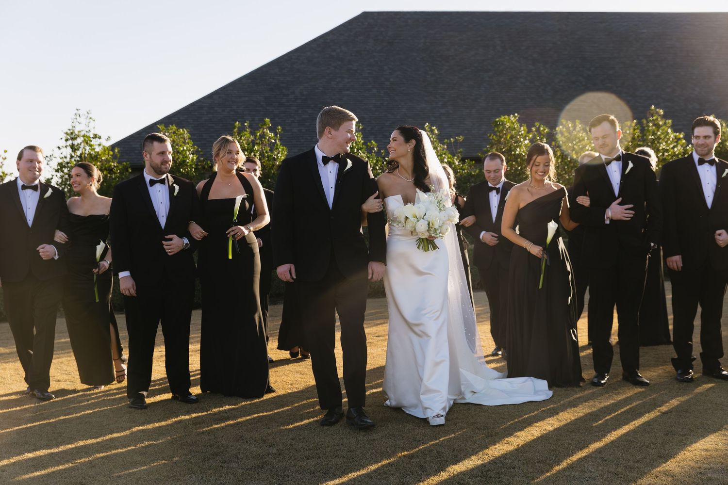Wedding party lined up outdoors during golden hour with long shadows.
