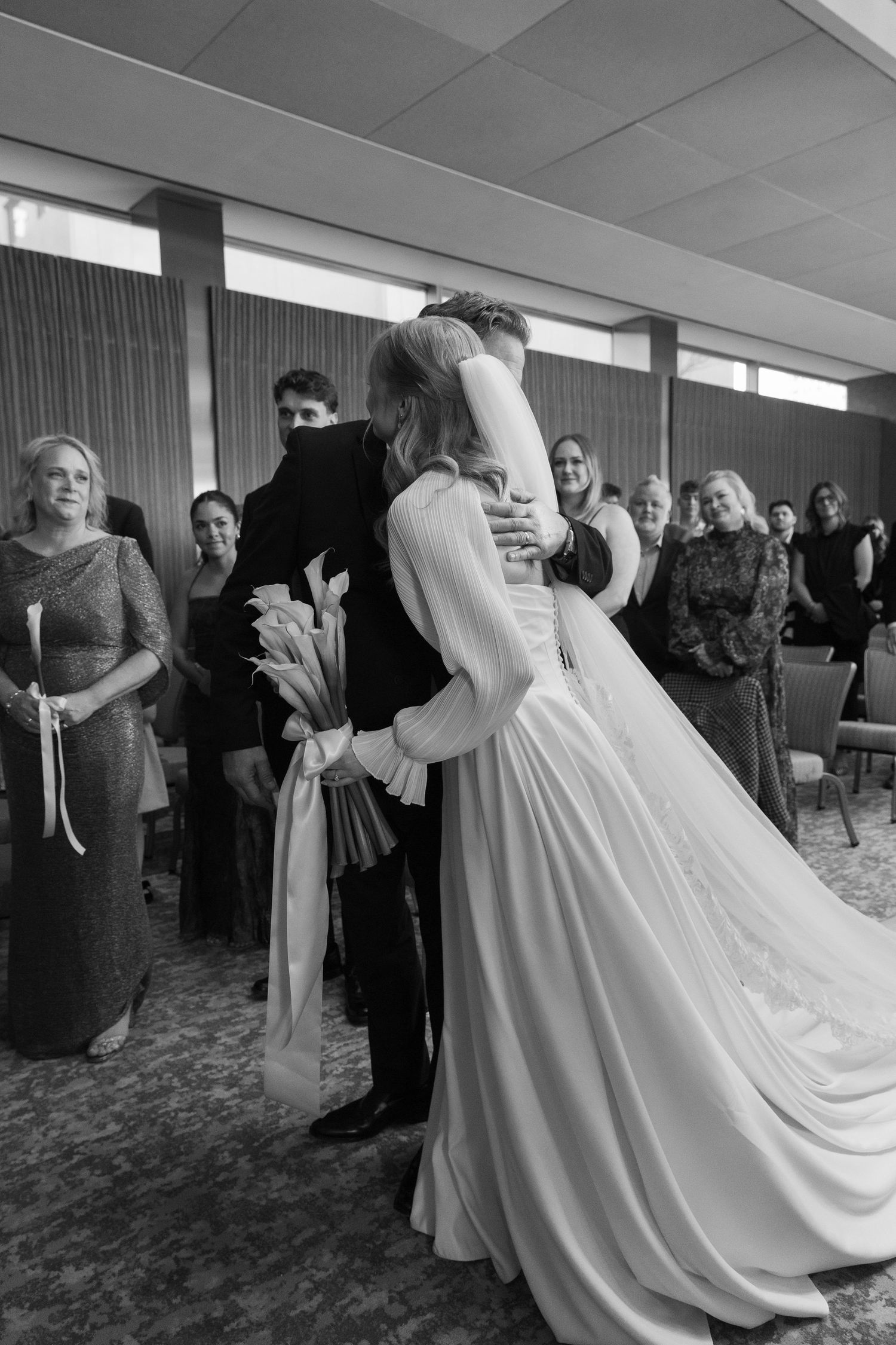 Wedding couple dancing together in an indoor reception venue with guests watching in the background.