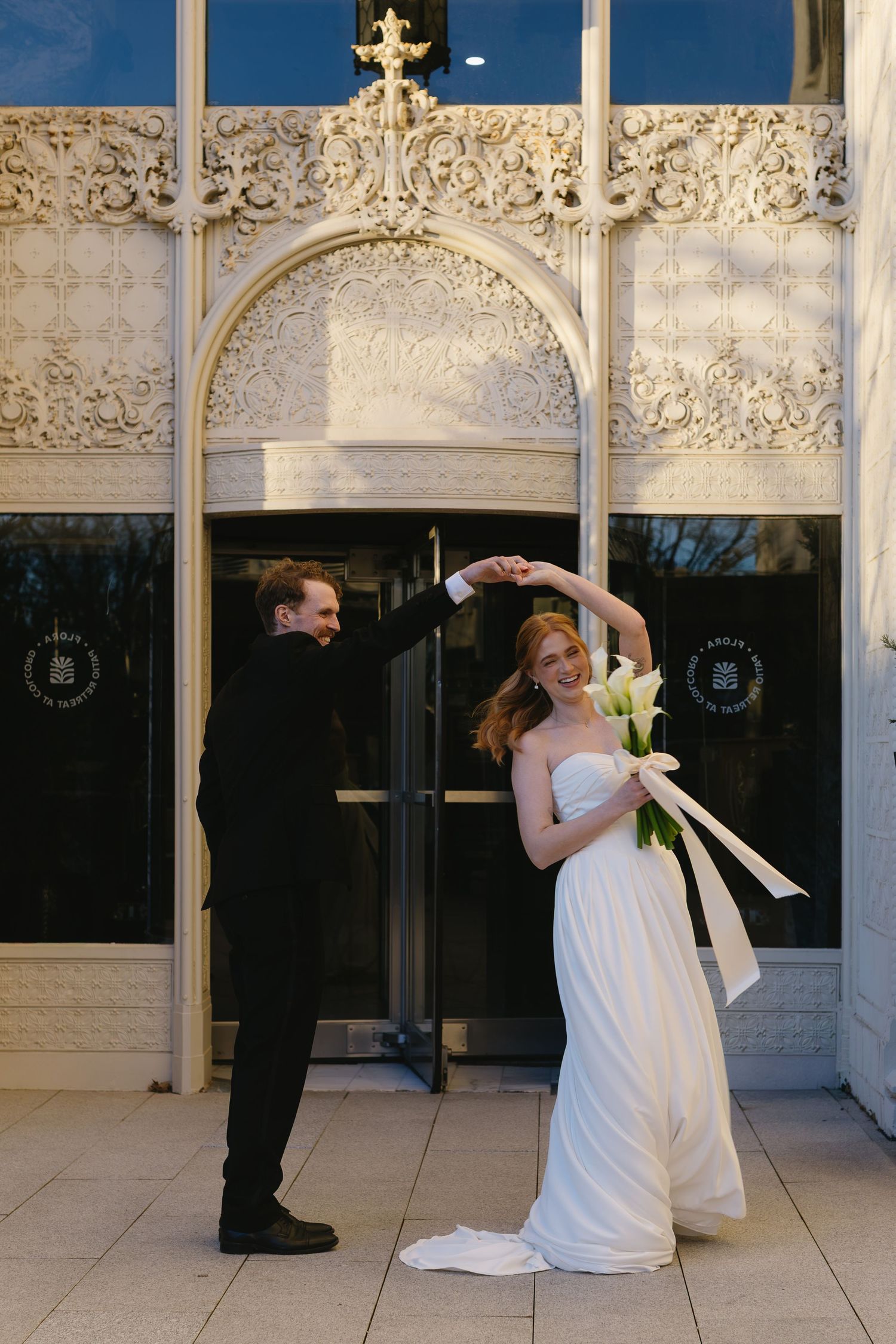 Bride and groom share a romantic moment against an ornate white architectural backdrop.