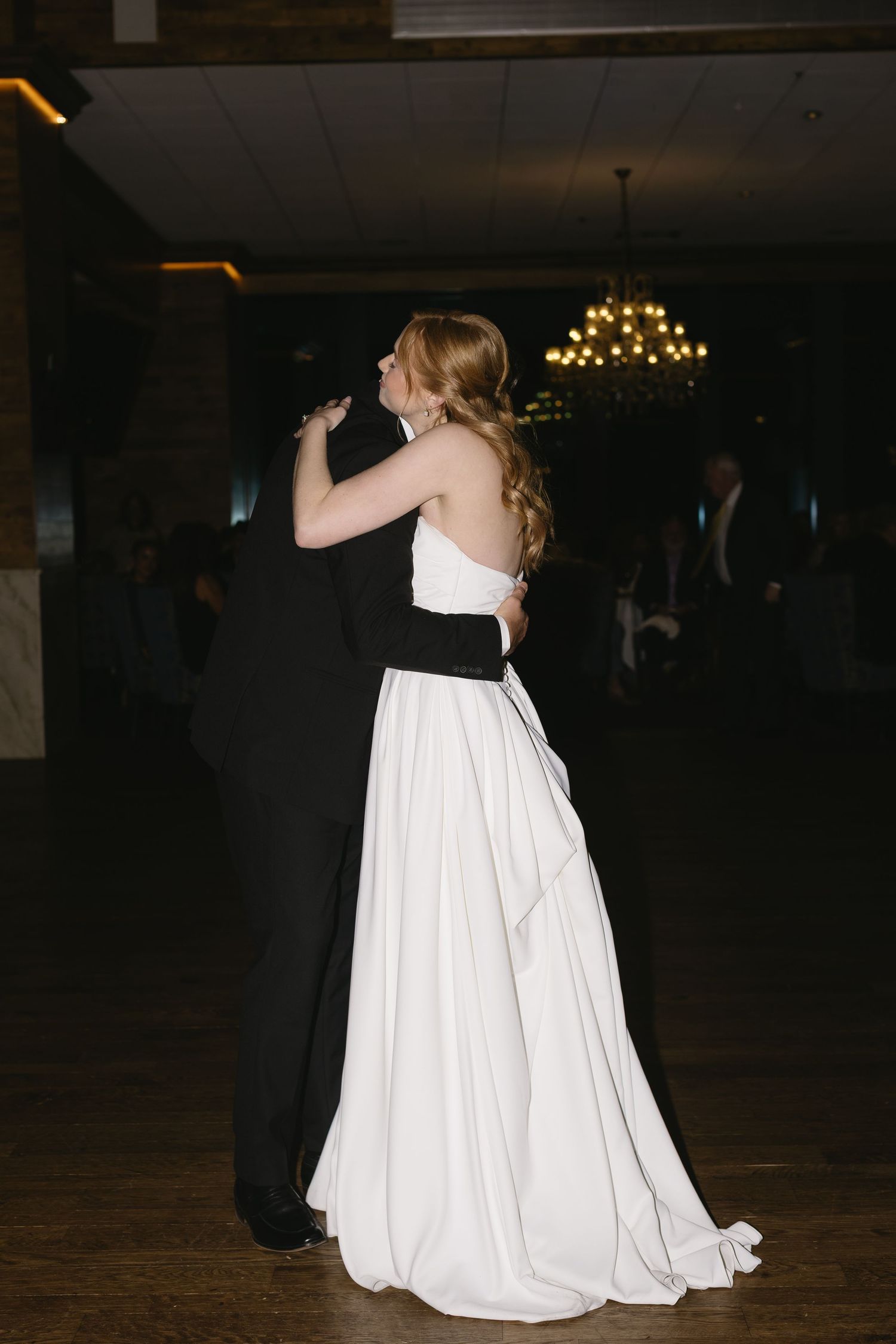 Wedding couple dances in dimly lit ballroom with flowing white gown.