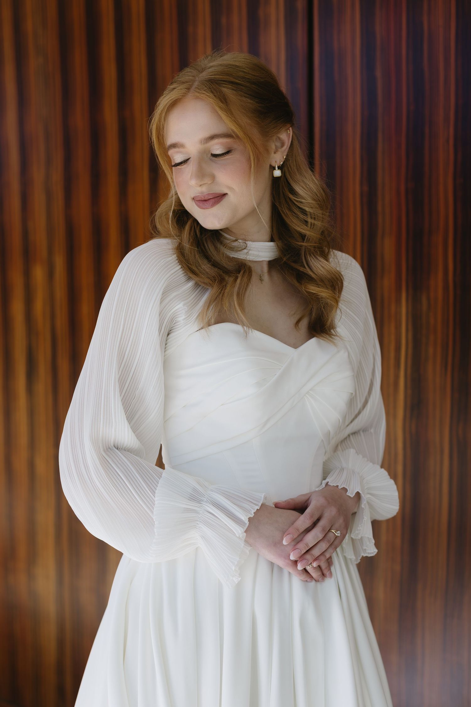 Classic white wedding gown with sheer bishop sleeves against wooden paneled wall.