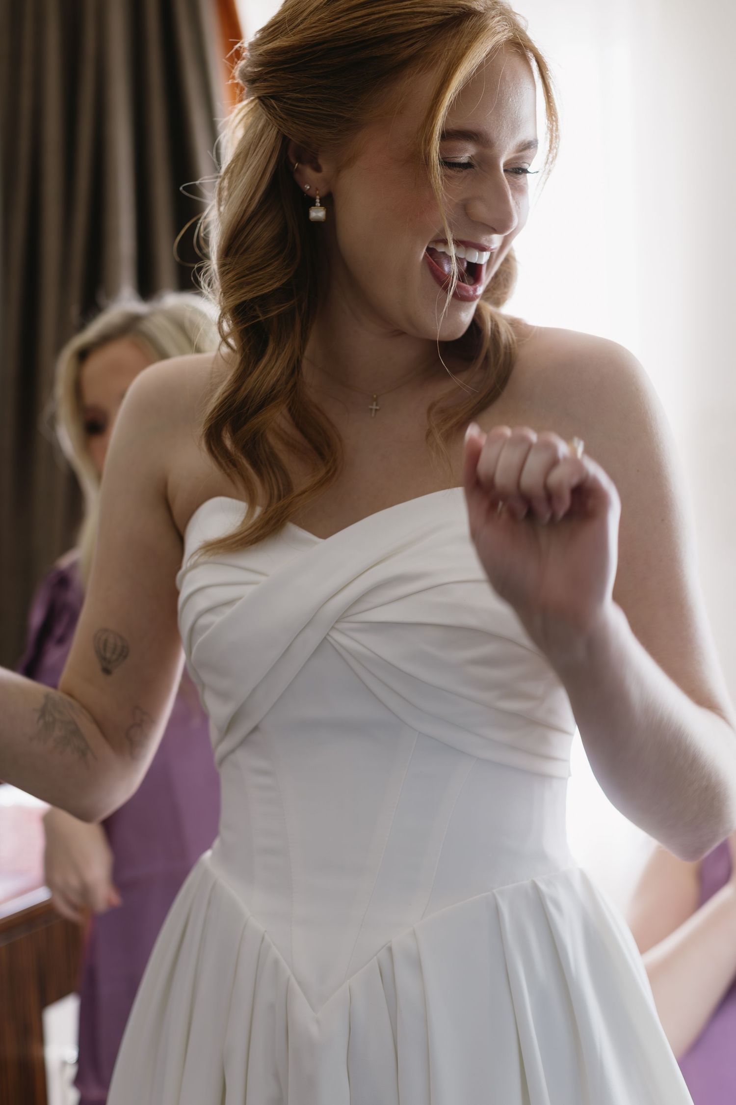 White wedding dress being fitted and adjusted during a joyful preparation moment.