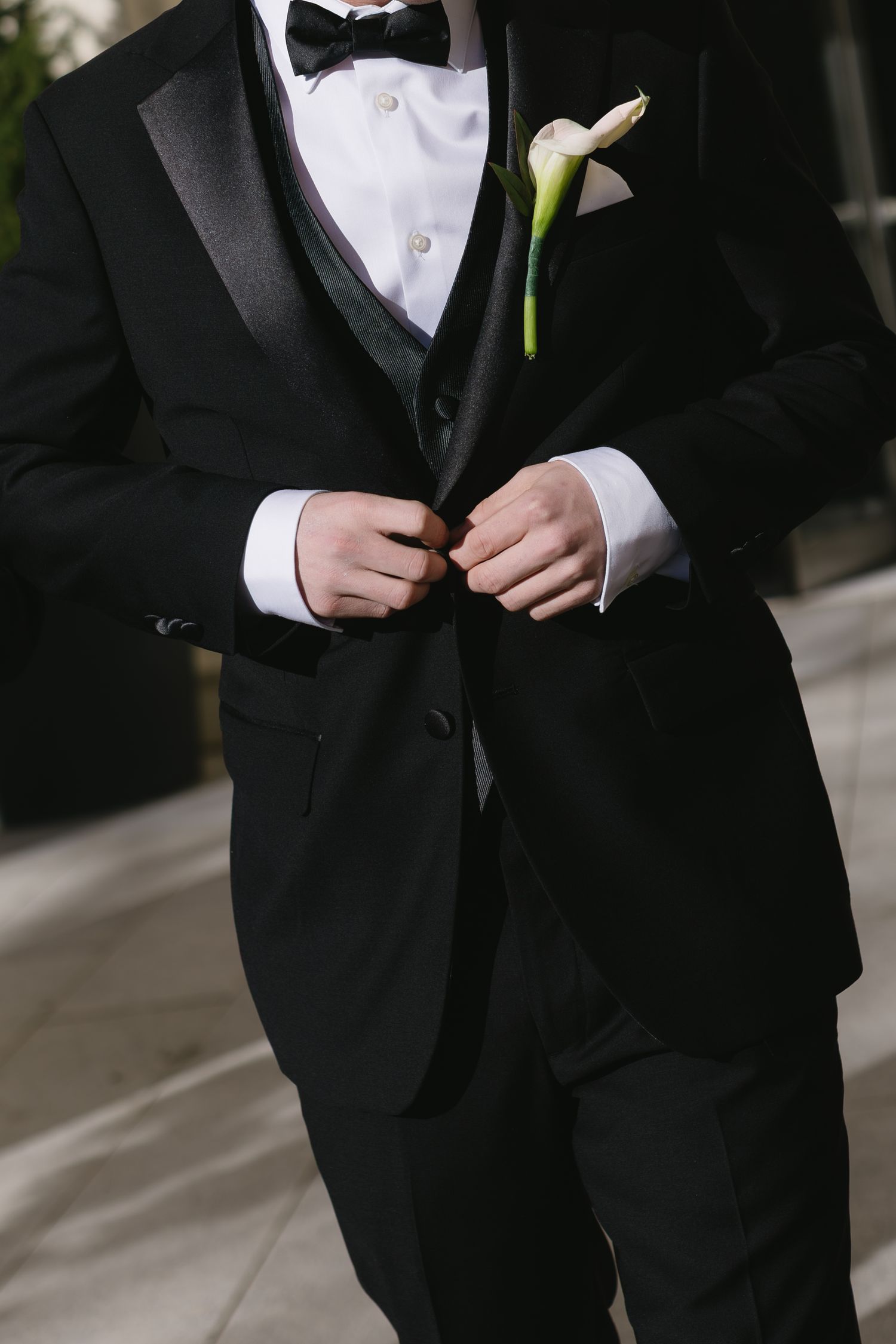 Close-up details of a groom's classic black tuxedo with white boutonniere.
