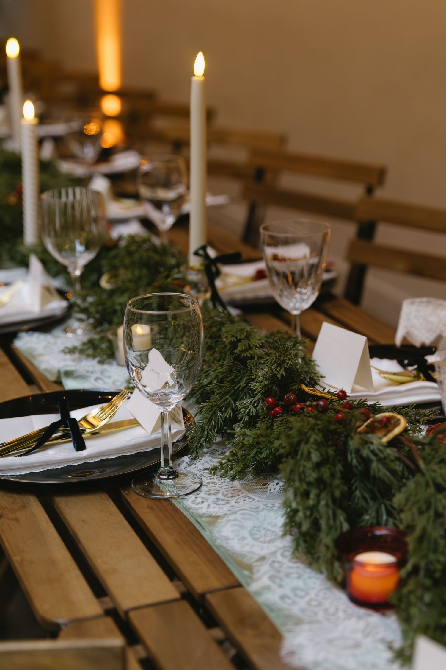 Festive wedding reception table with evergreen garland, candles, and elegant place settings.