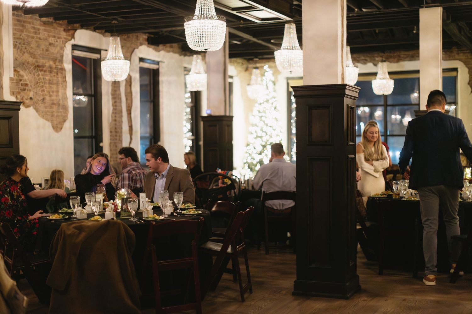 Interior view of a rustic brick venue space with exposed beams and scattered tables.