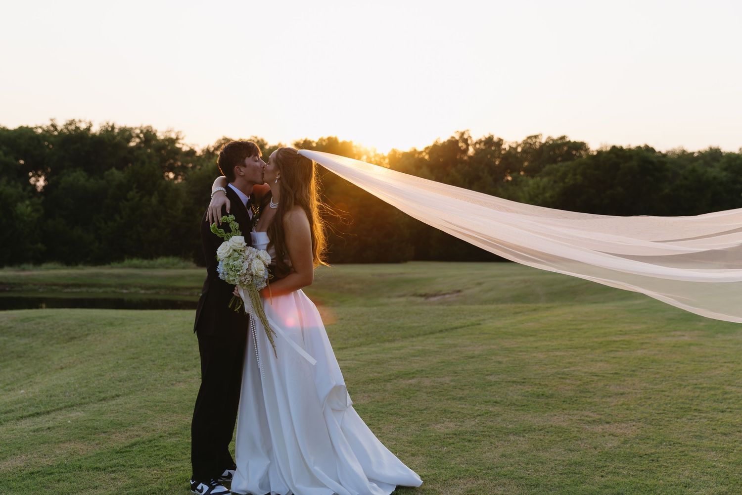 Romantic sunset wedding ceremony on a grassy lawn with flowing white fabric blowing in the breeze.