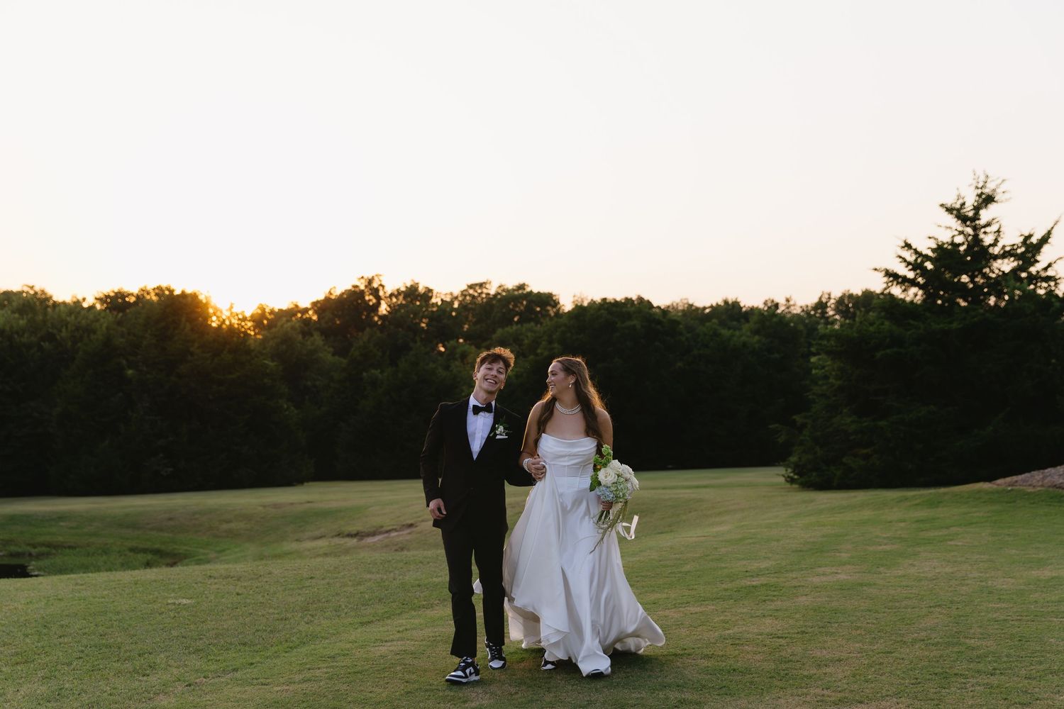 Newlyweds walking together on a golf course at sunset.