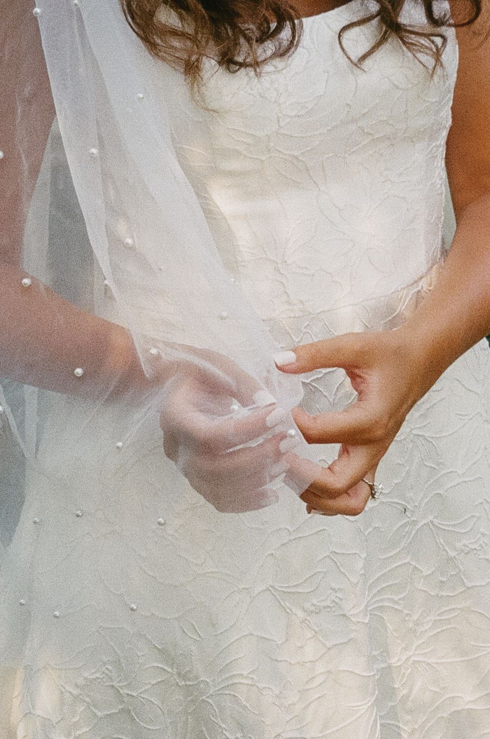 Close-up view of intricate white lace details on a wedding dress, showing delicate floral patterns and beading.