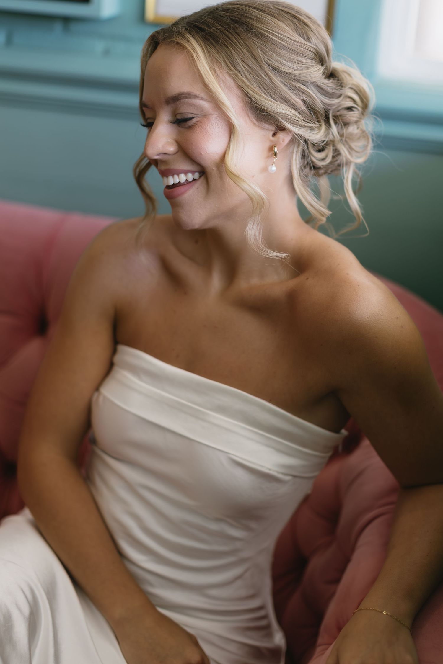 Candid bridal portrait showing radiant smile against turquoise wall and pink sofa.