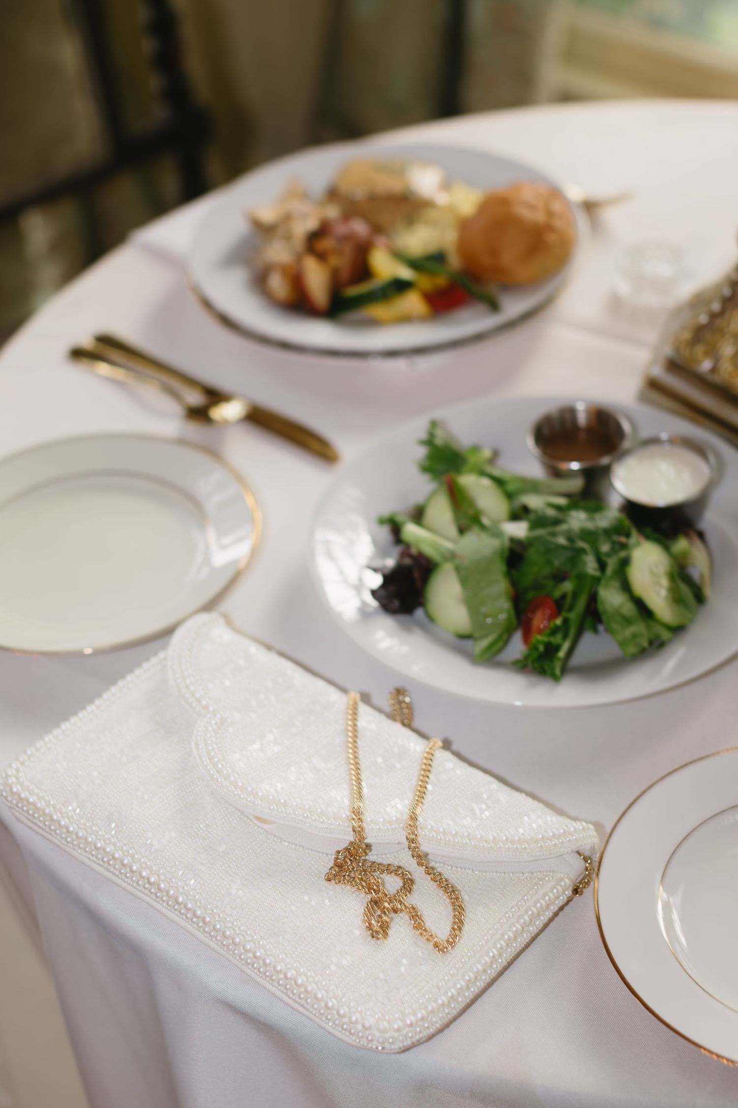 Elegant place setting with salad plate, white tablecloth and gold necklace accessory.