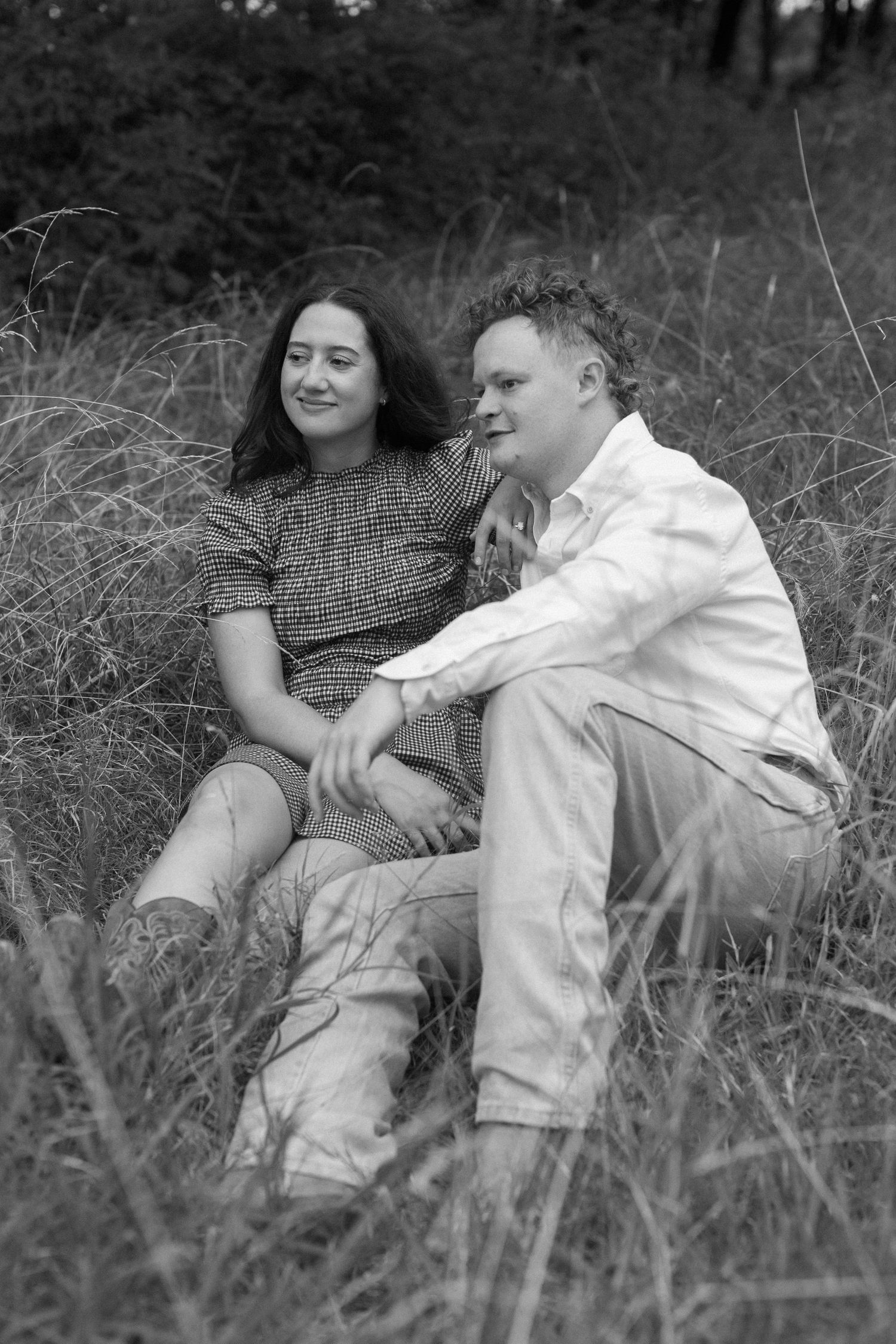 Couple relaxes intimately in tall grass field during a black and white photoshoot.