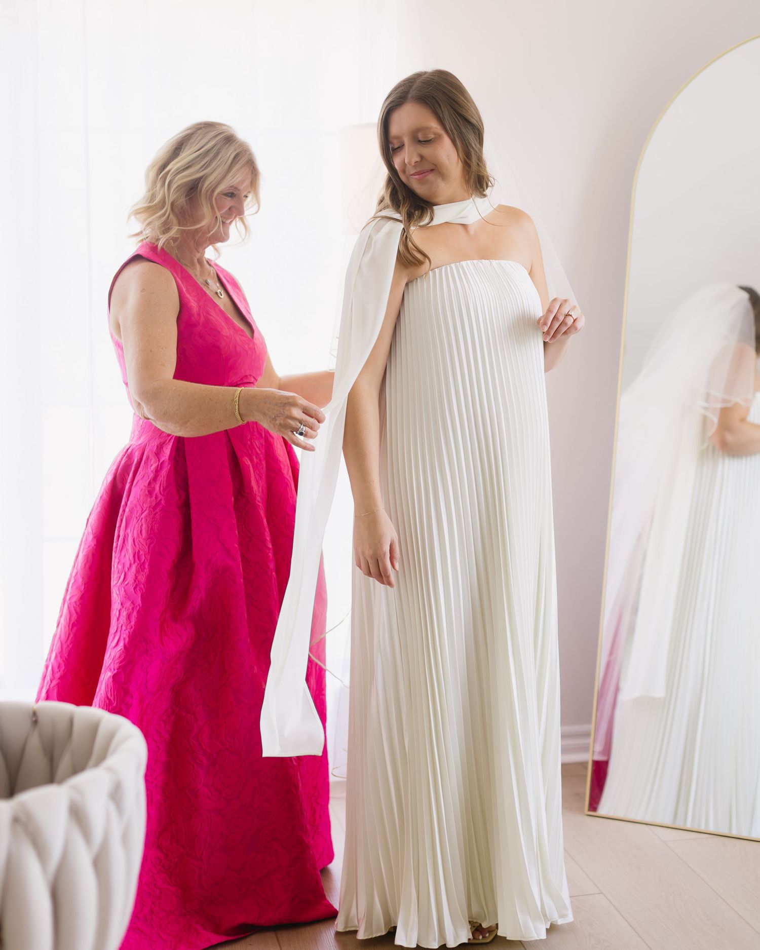 Wedding dress preparation scene with white pleated gown and pink accent dress.