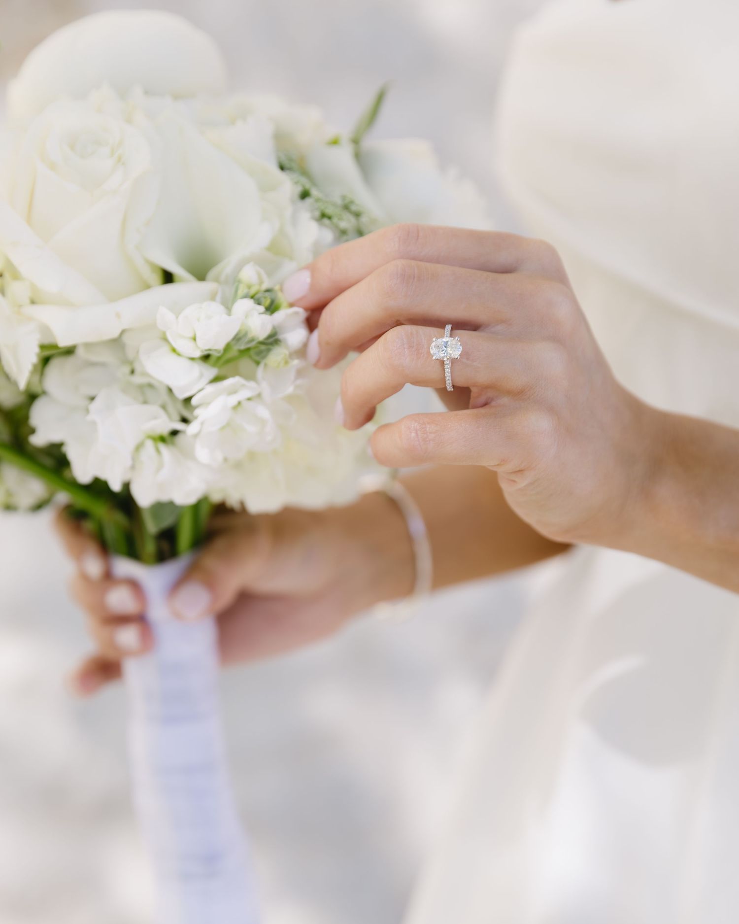 Close-up of hands holding white floral bouquet with diamond engagement ring prominently displayed.