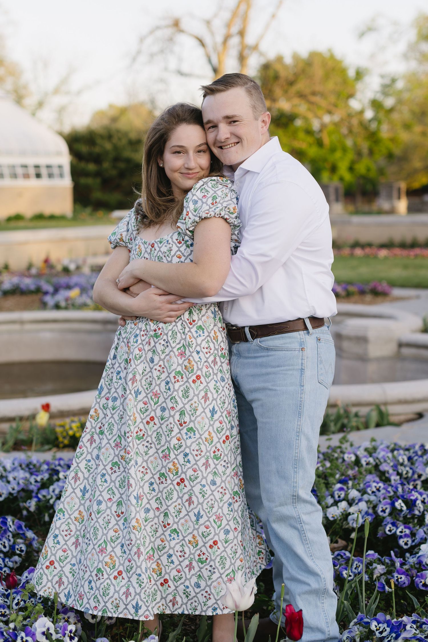 A couple poses together among purple pansies in a well-manicured garden.