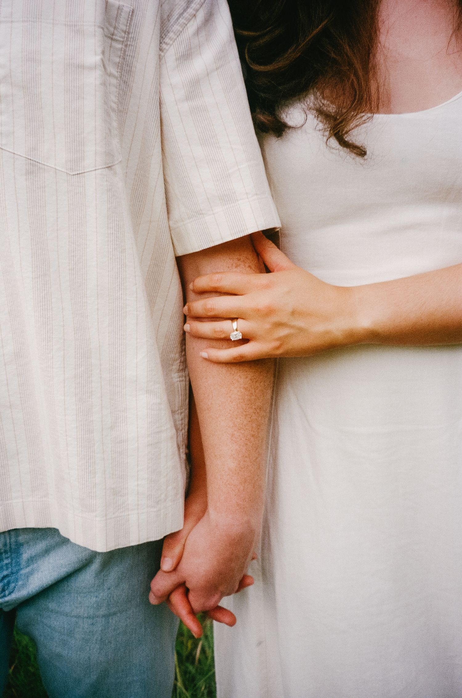 Close-up details of hands holding each other against white clothing showing tenderness and intimacy.