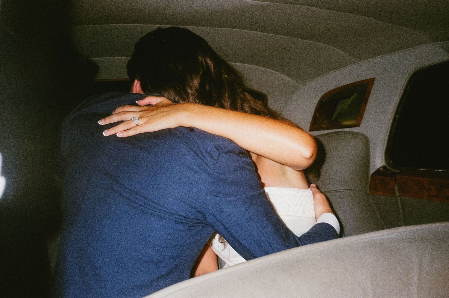 A couple in blue attire embrace while dancing in a dimly lit room.