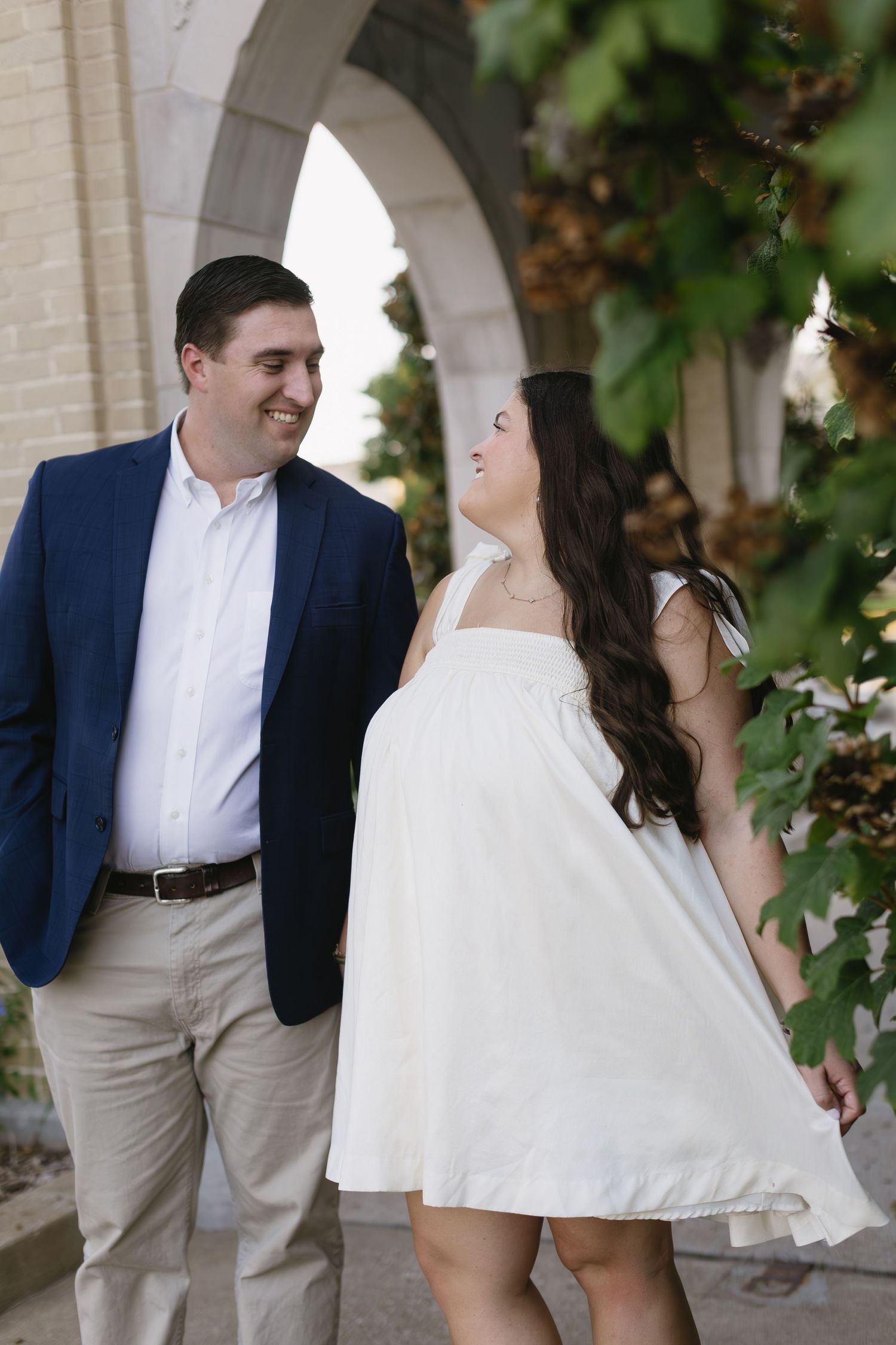 A romantic engagement session under an arched walkway with ivy and architectural details.