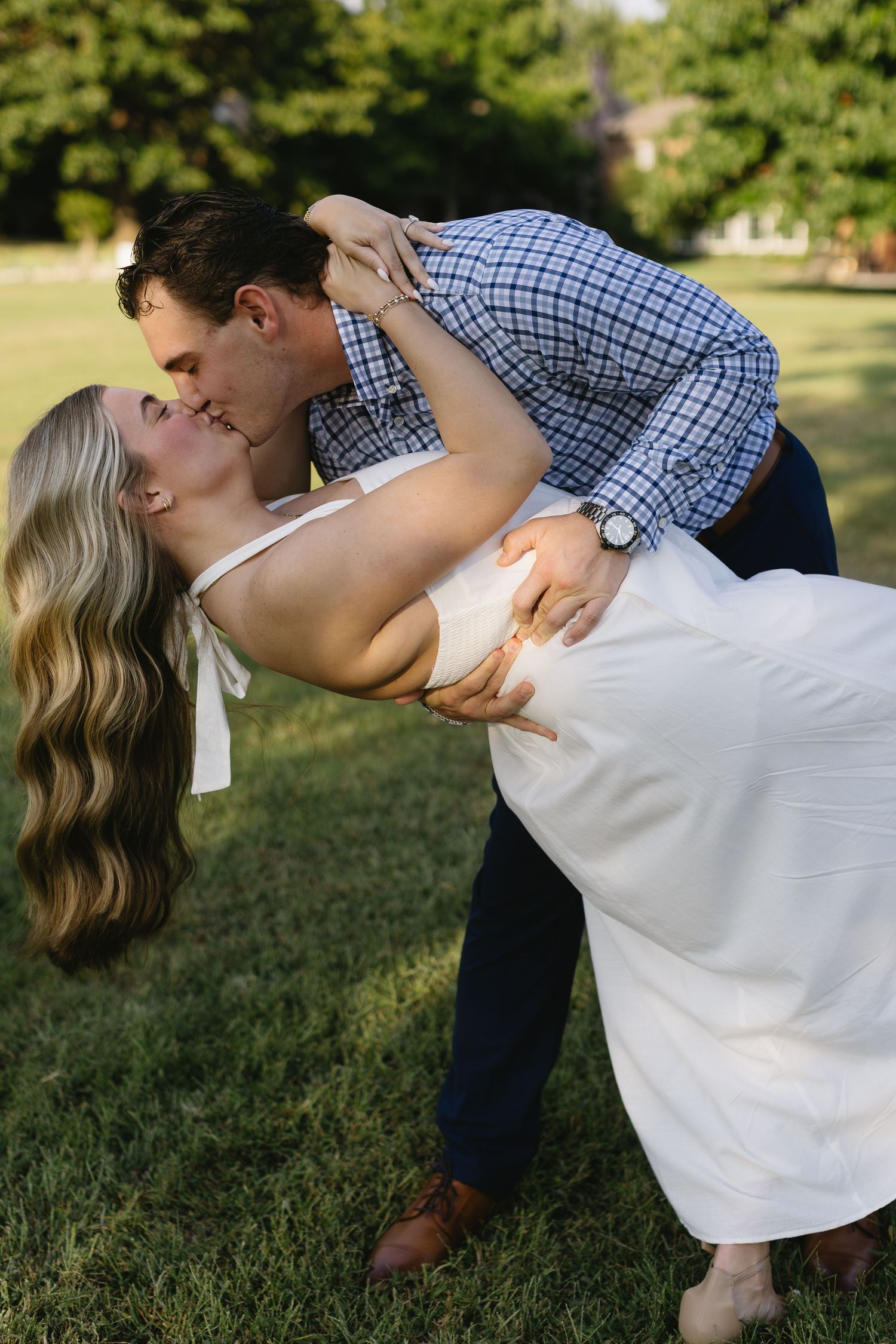 Romantic dip pose on a sunlit lawn wearing white and blue plaid clothing.