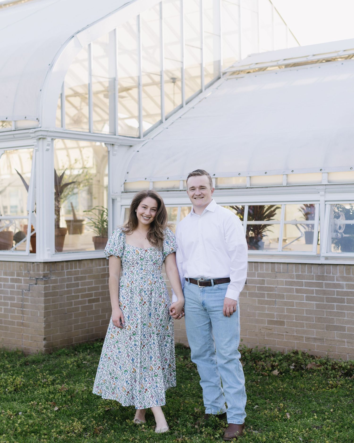 Family poses together in front of white greenhouse wall with brick base and wooden door frame.